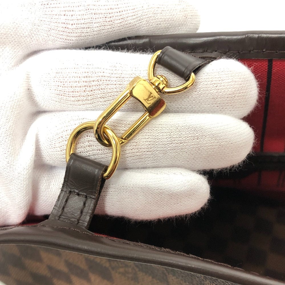 Close-up of a gold handbag clasp with a brand logo, held by a gloved hand.