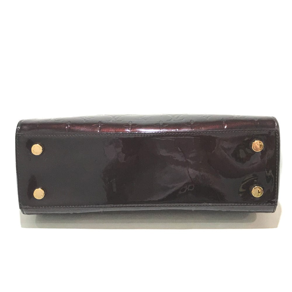 Black patent leather clutch bag with gold hardware on a white background