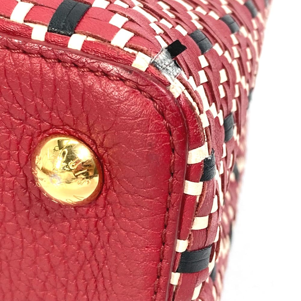 Close-up of a red textured handbag with a gold button and black and white checkered pattern.