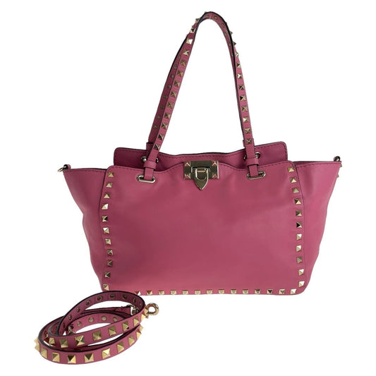 Pink handbag with gold studs and matching strap on a white background