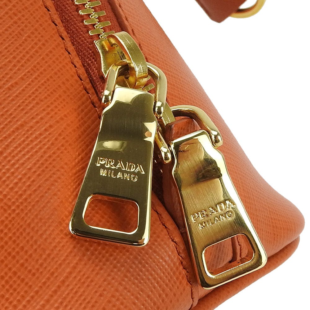 Close-up of a Prada handbag zipper with gold hardware on an orange background