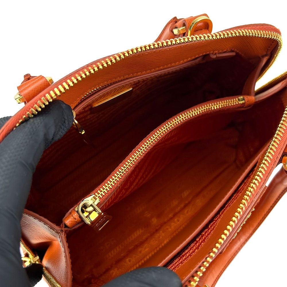 Brown leather handbag with gold zipper and clasp, held by a gloved hand.