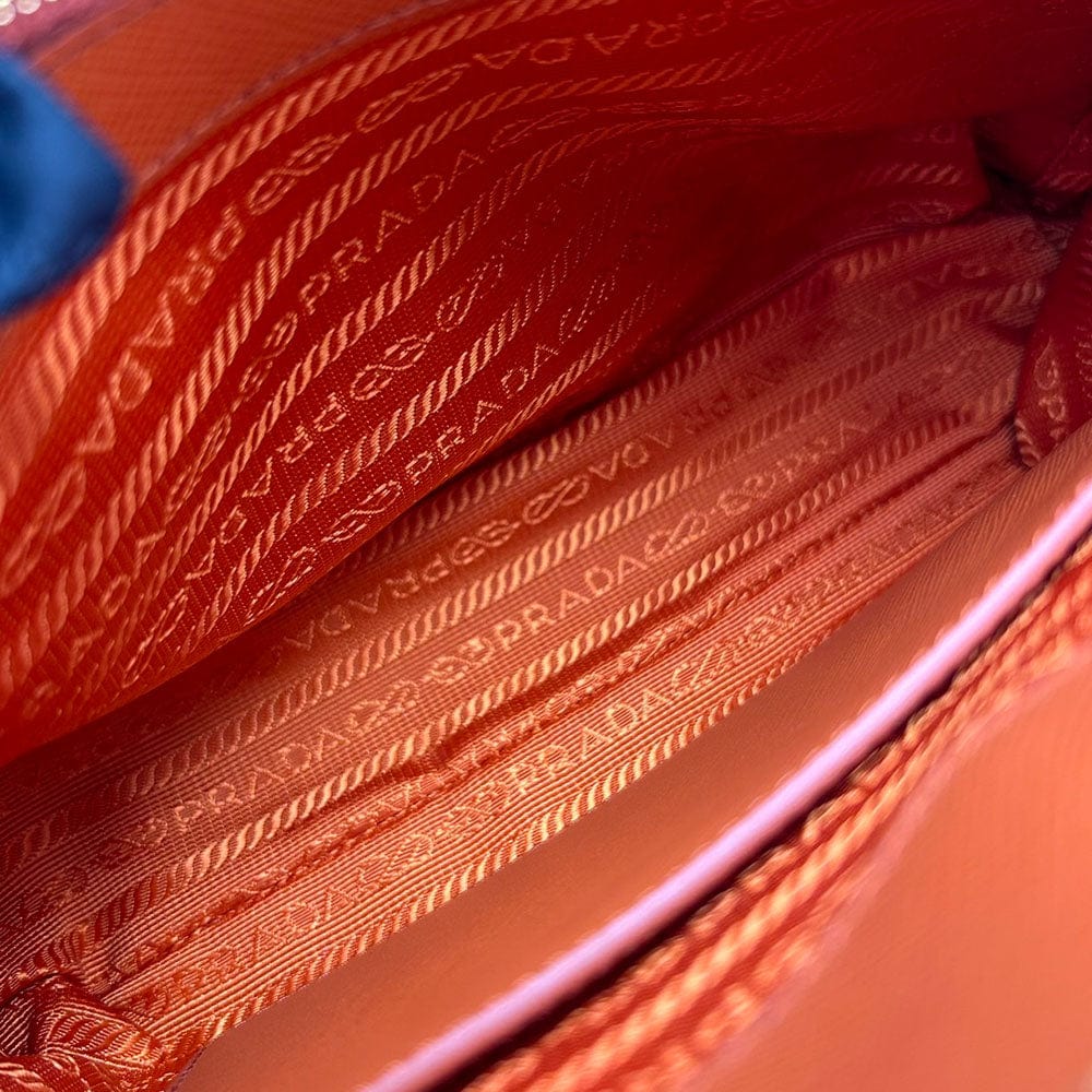 Close-up of an orange Prada handbag with visible branding.