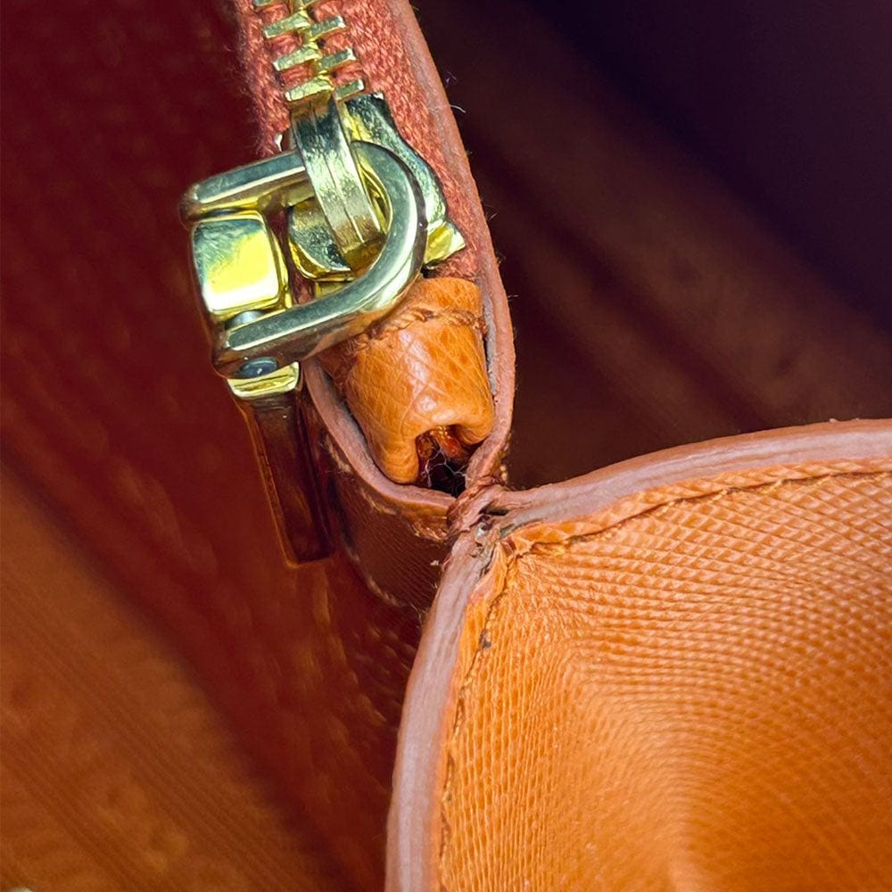 Close-up of a gold zipper on an orange leather bag.