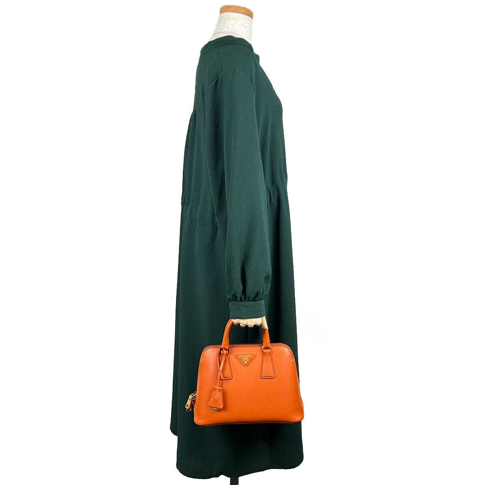 Mannequin wearing a green dress holding an orange handbag on a white background