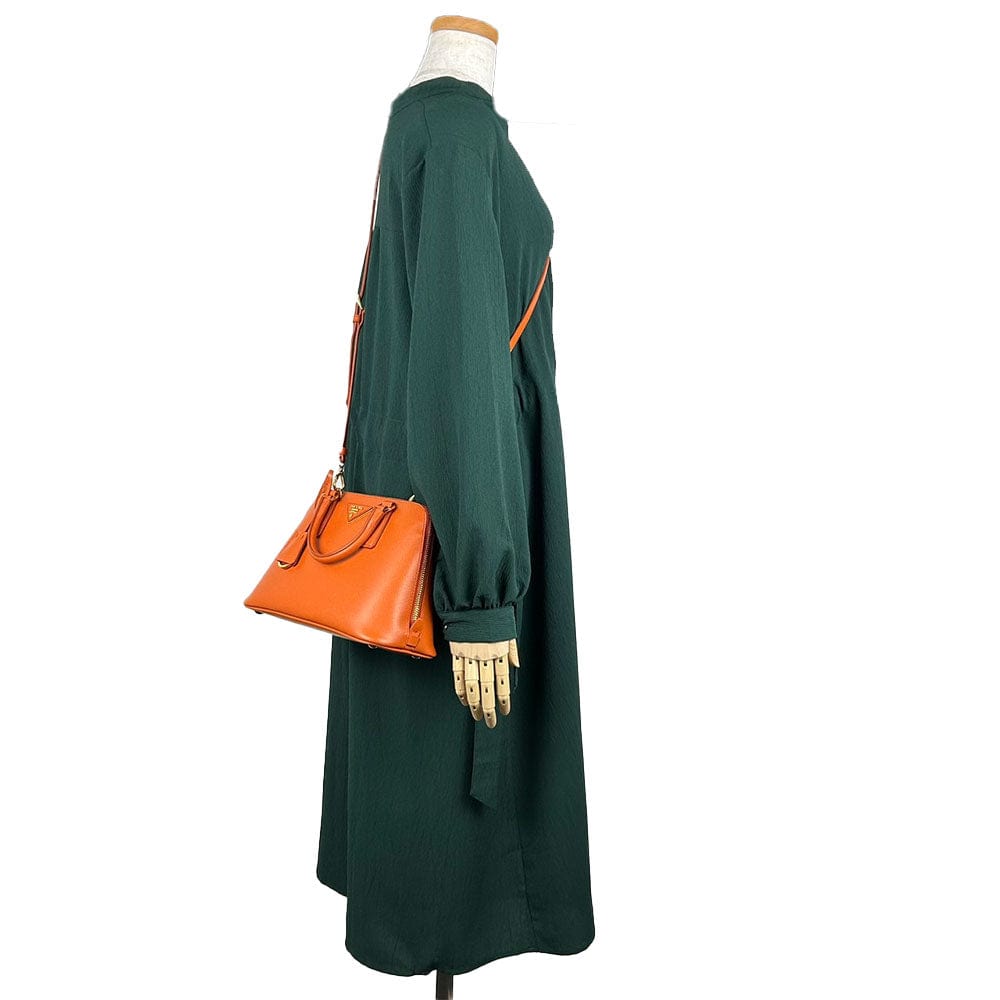Green dress with orange handbag on a mannequin against a white background