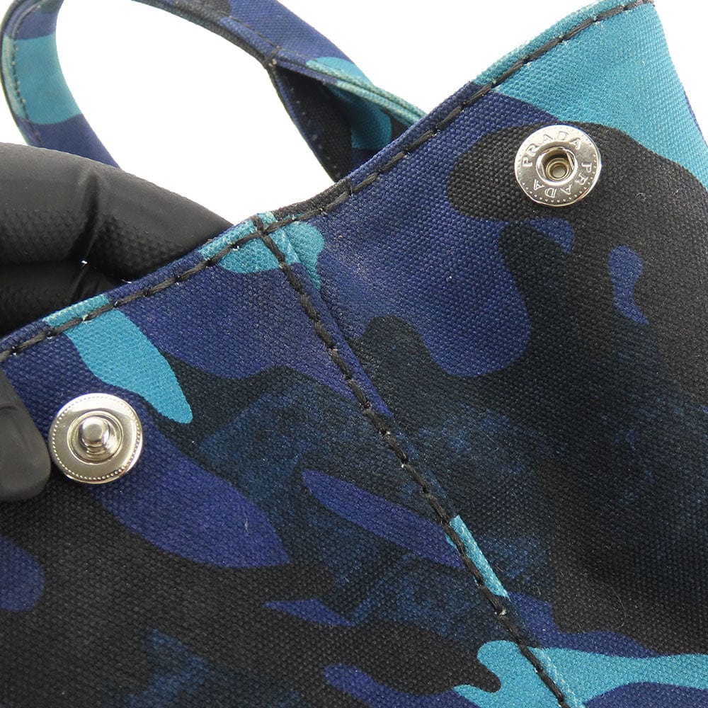 Close-up of a blue camouflage shoe with metal buttons, worn by a person wearing black gloves.