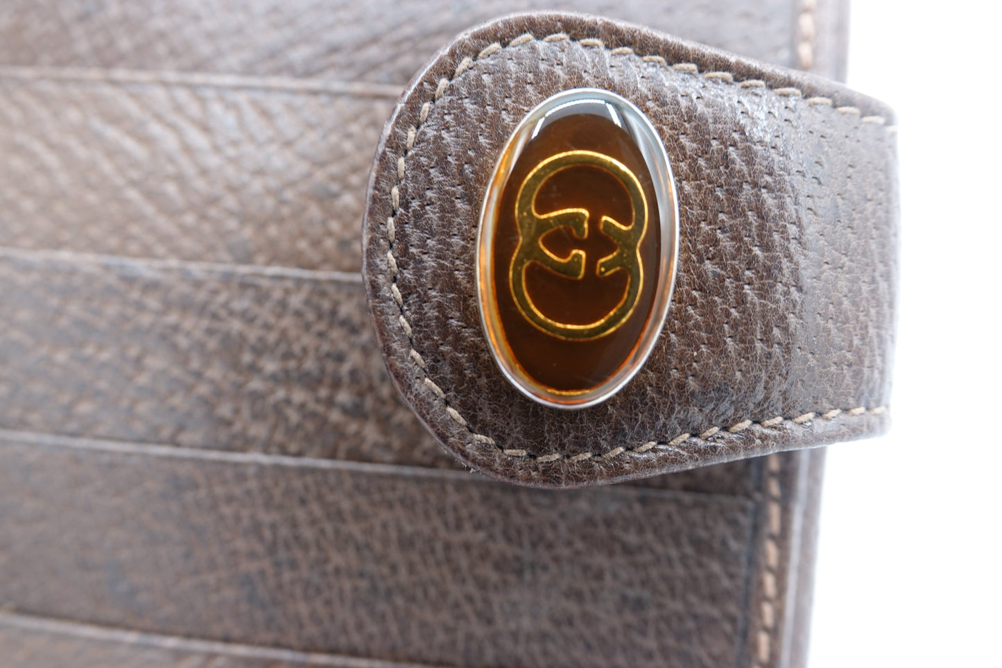 Close-up of a brown leather bag with a gold and silver logo.