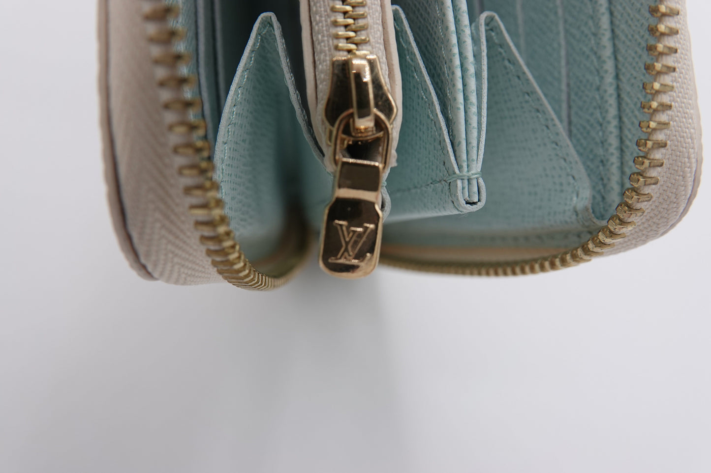 Close-up of a light blue wallet with gold zipper and logo on a white background