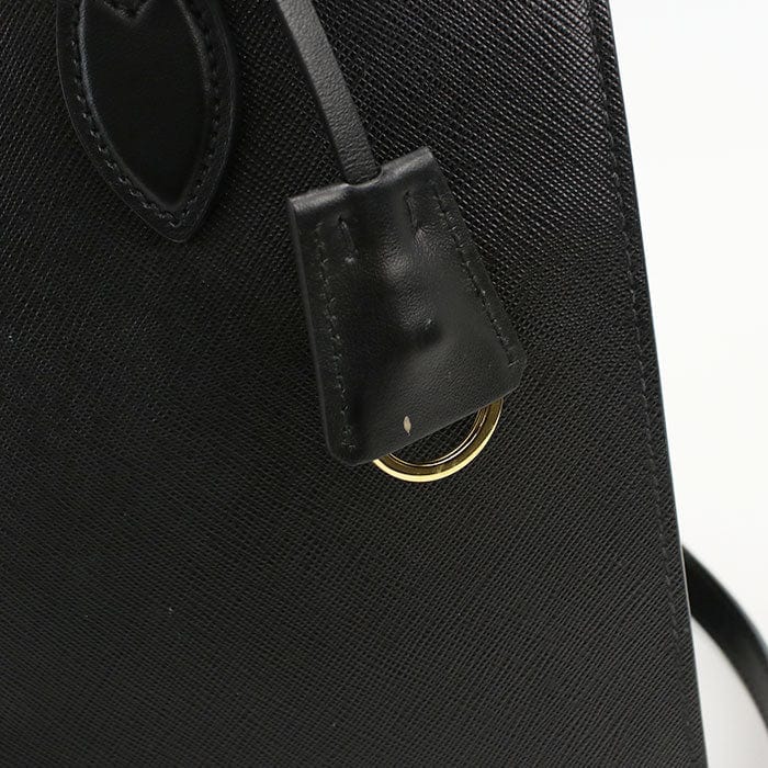 Close-up of a black textured bag with a gold ring and leather tag.