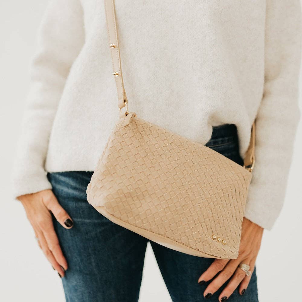 Beige textured handbag held by a person wearing a white sweater and blue jeans.