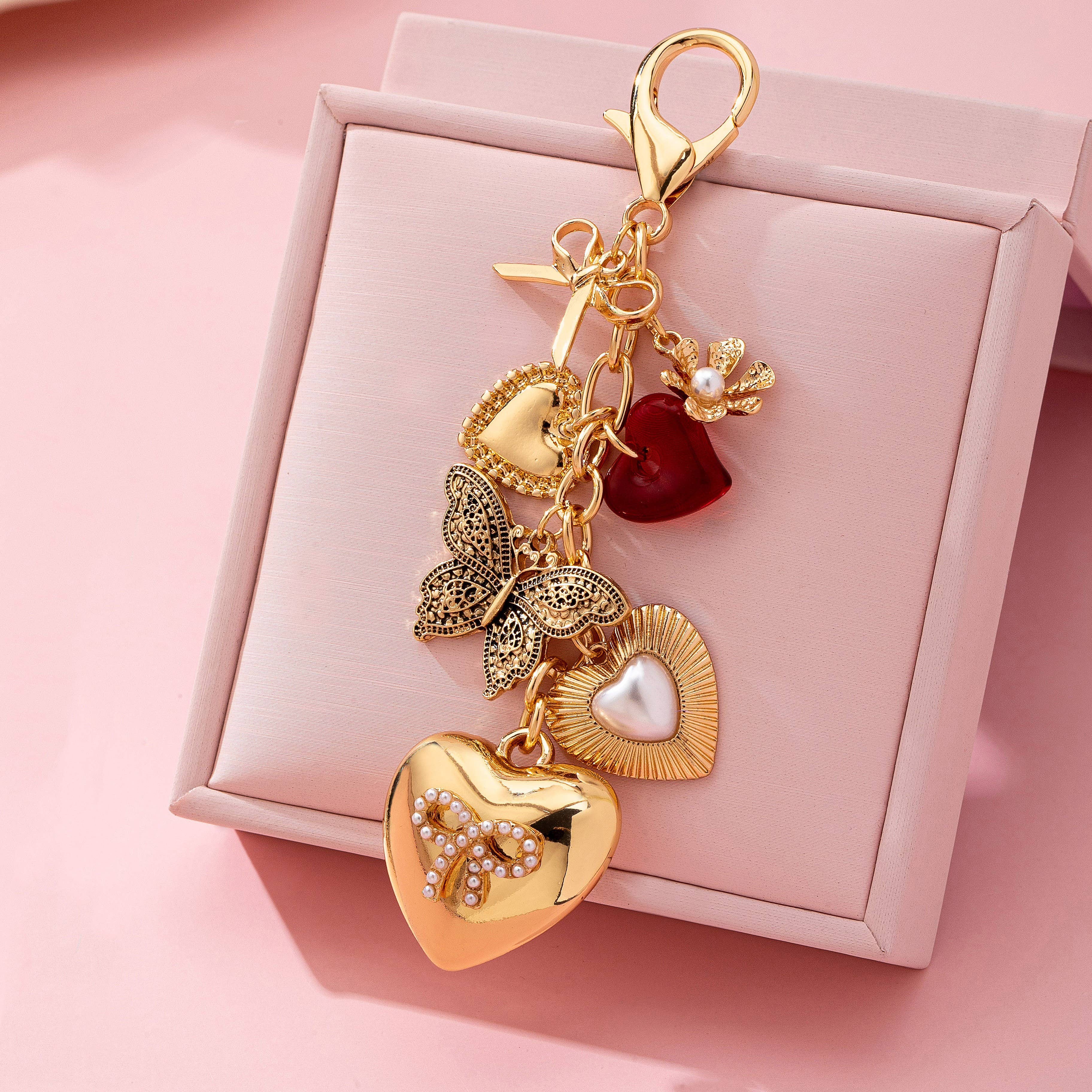 Gold keychain with heart and butterfly charms on a pink box background