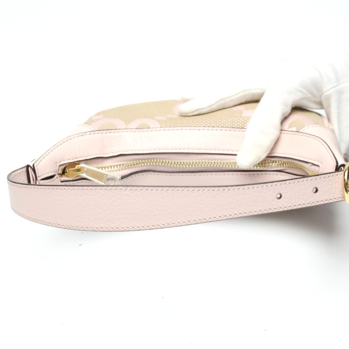 Pink handbag with gold zipper being held by a gloved hand on a white background