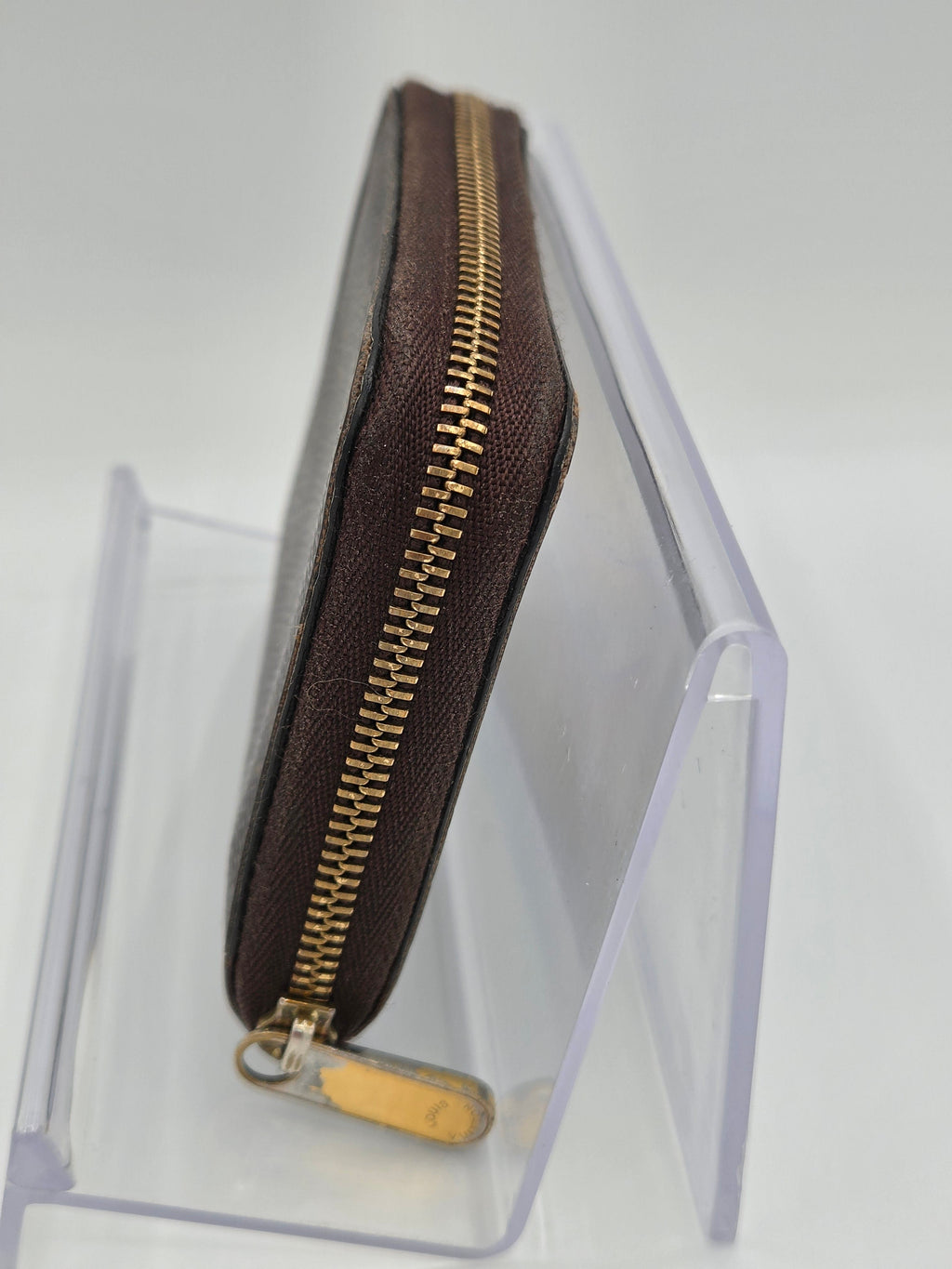 Brown zipper pouch with gold zipper on a clear stand against a white background