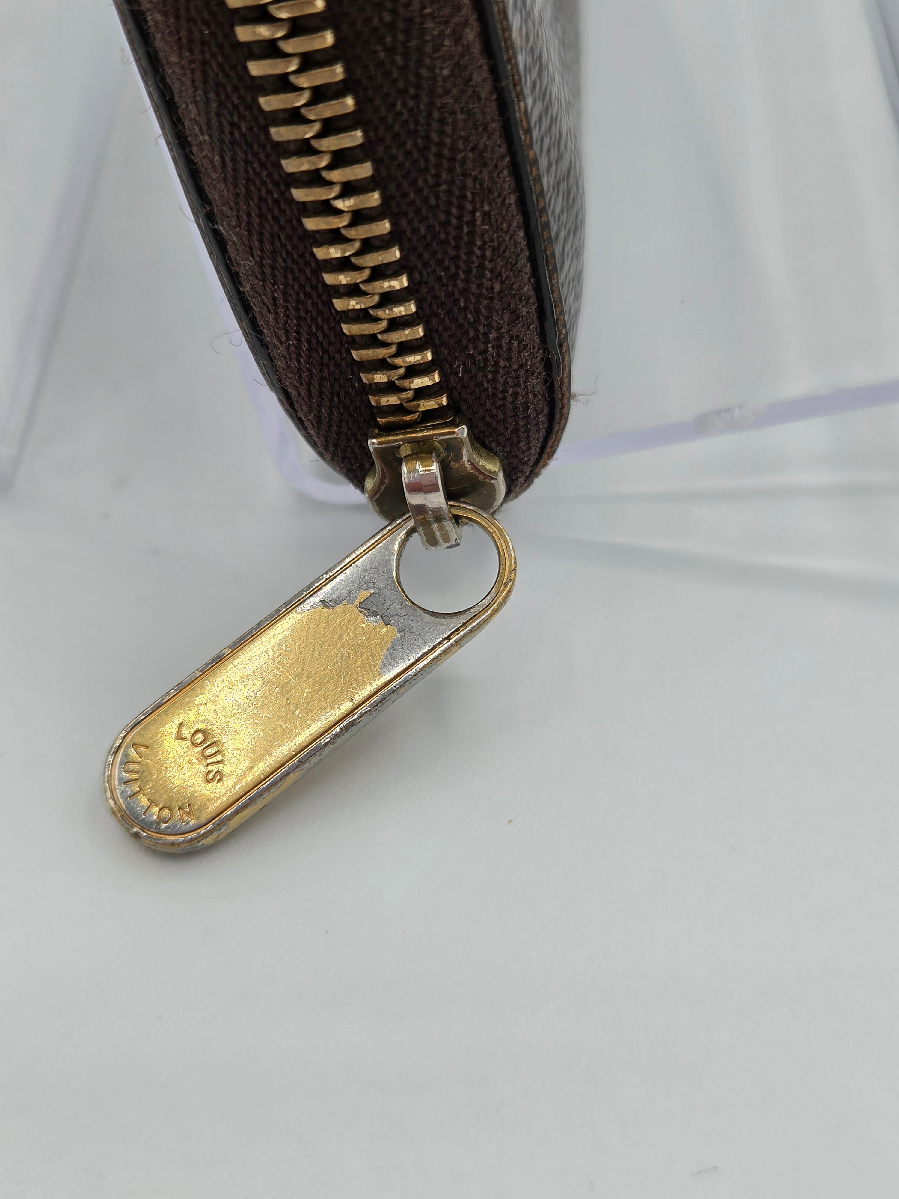 Close-up of a brown wallet with a gold zipper pull on a white background