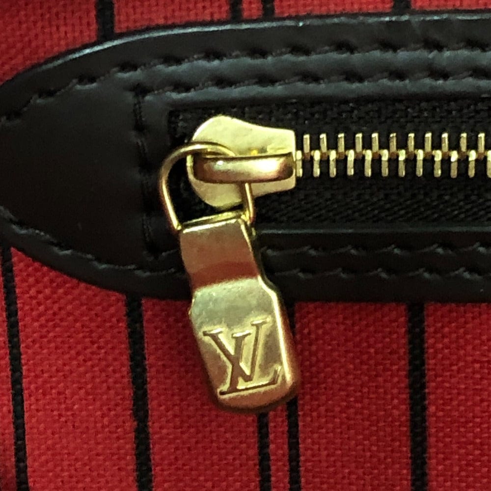 Close-up of a gold zipper pull on a red and black striped bag with a brand logo.