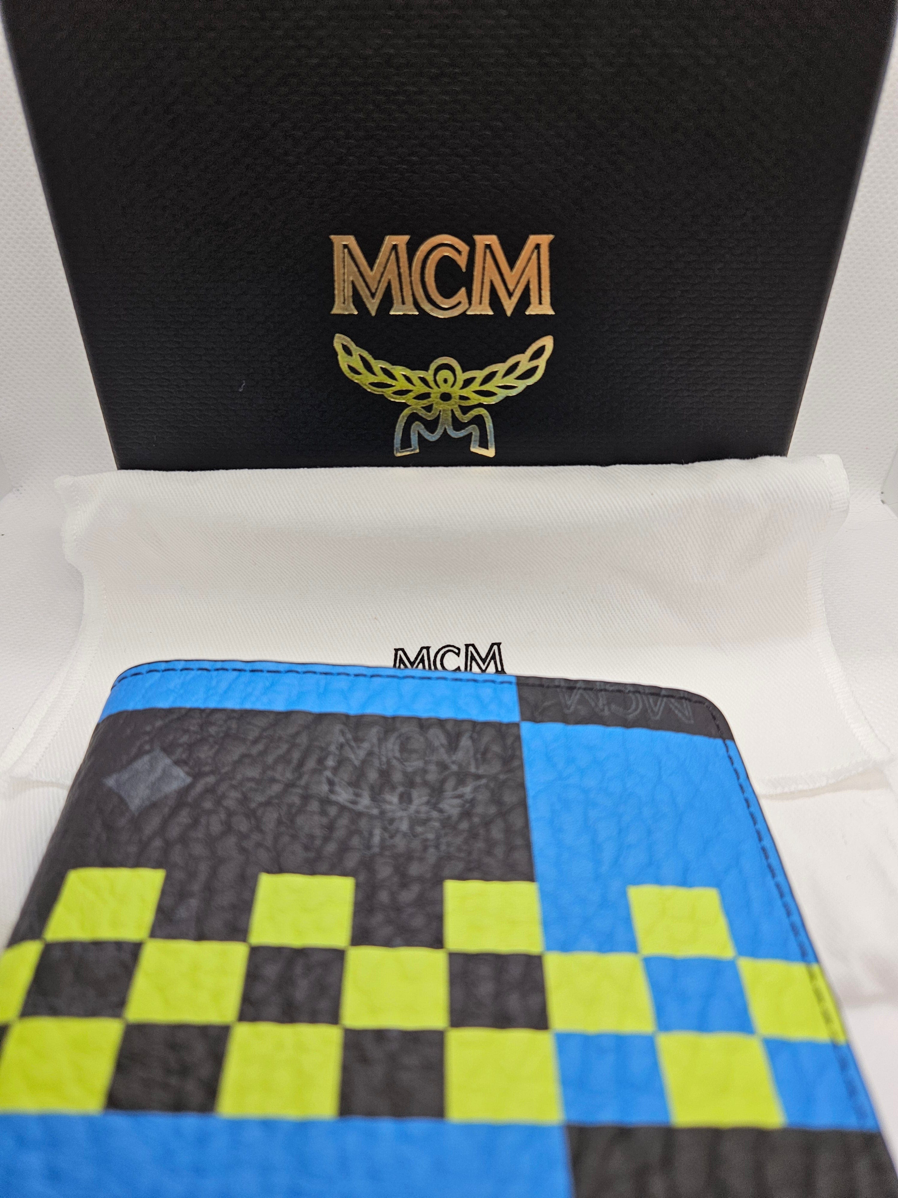 Two MCM wallets, one black with gold logo and the other checkered blue and green, on a white background.