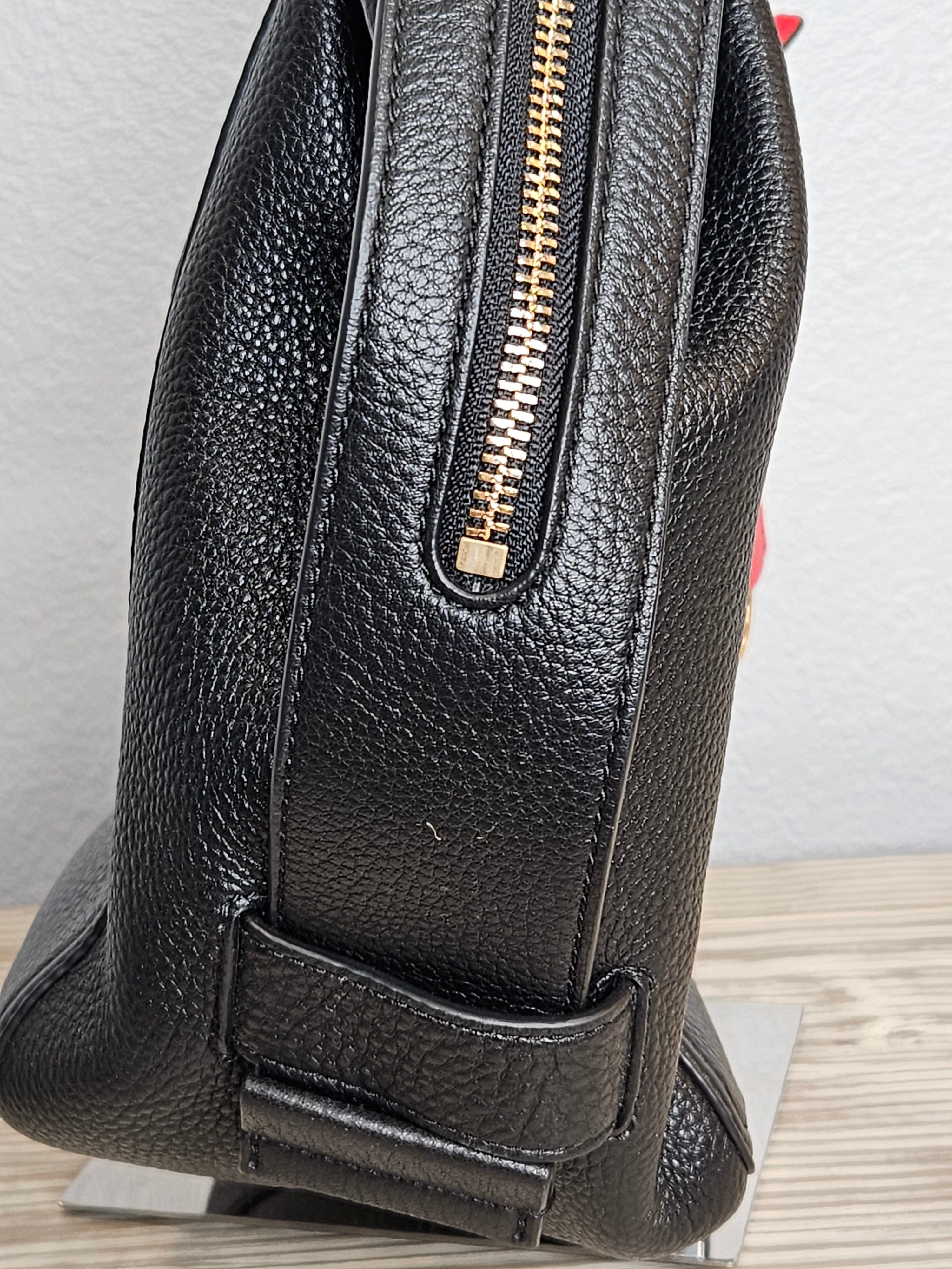 Black leather backpack with gold zipper on a wooden surface.