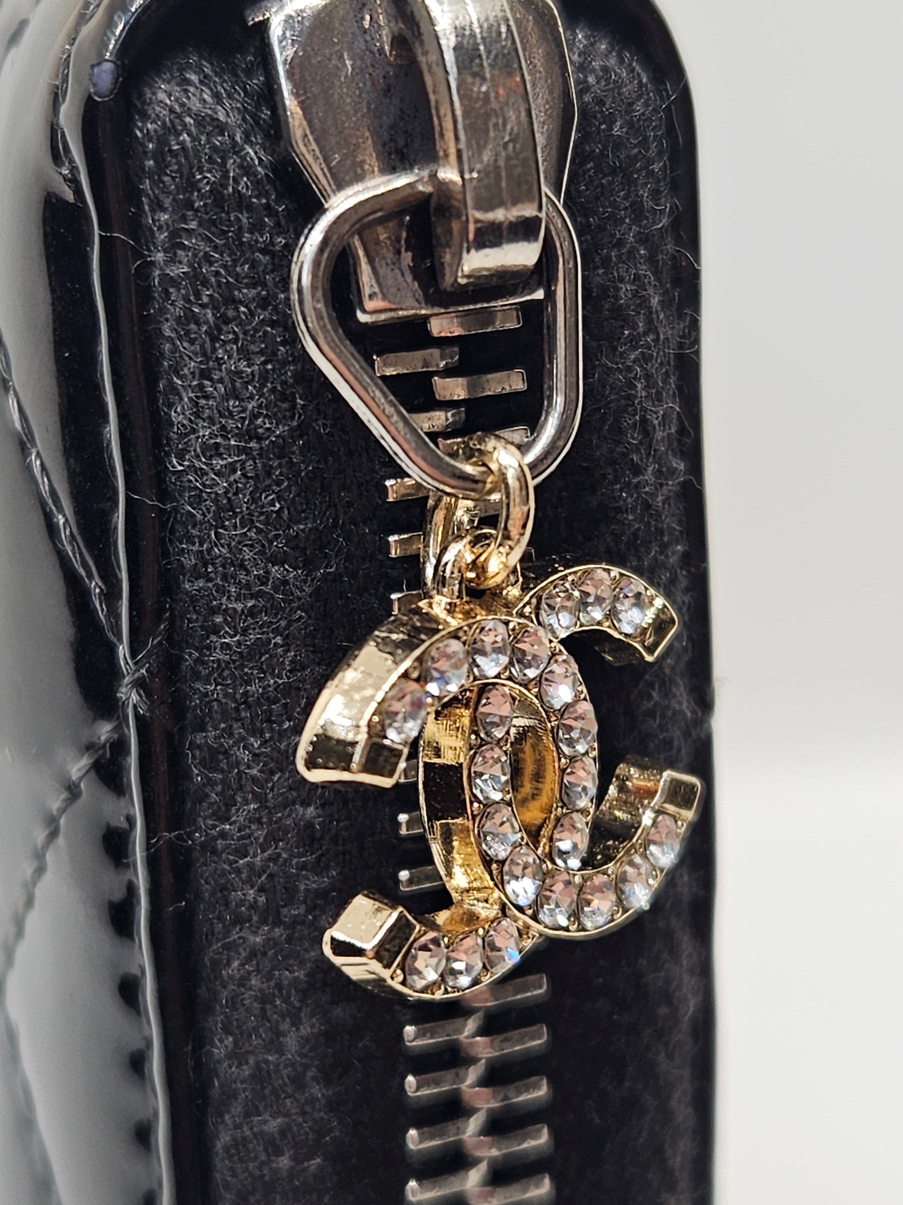 Gold and silver Chanel logo charm on a black leather surface