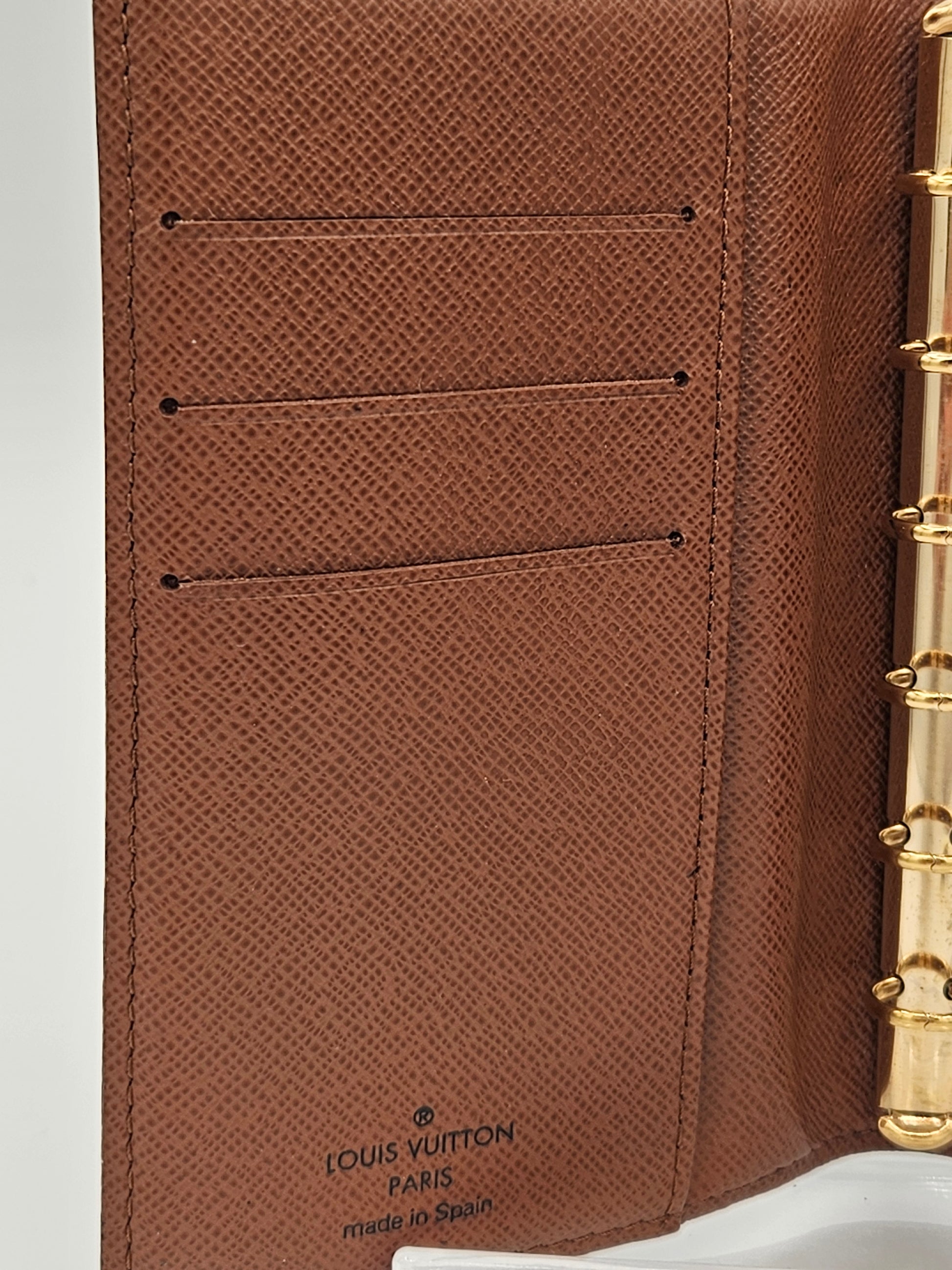 Brown textured leather product with gold accents and visible brand logo.