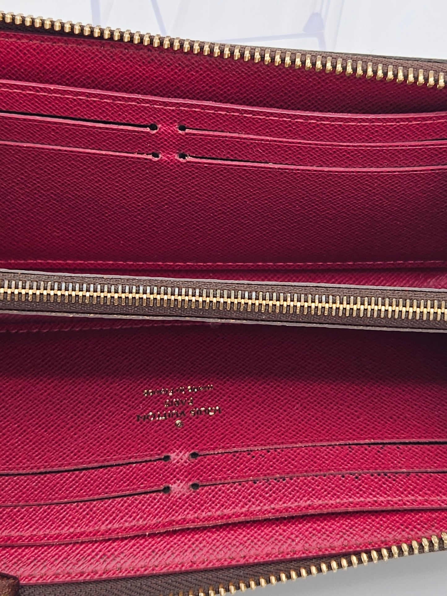 Close-up of a red textured bag with a gold zipper, featuring a brand logo.