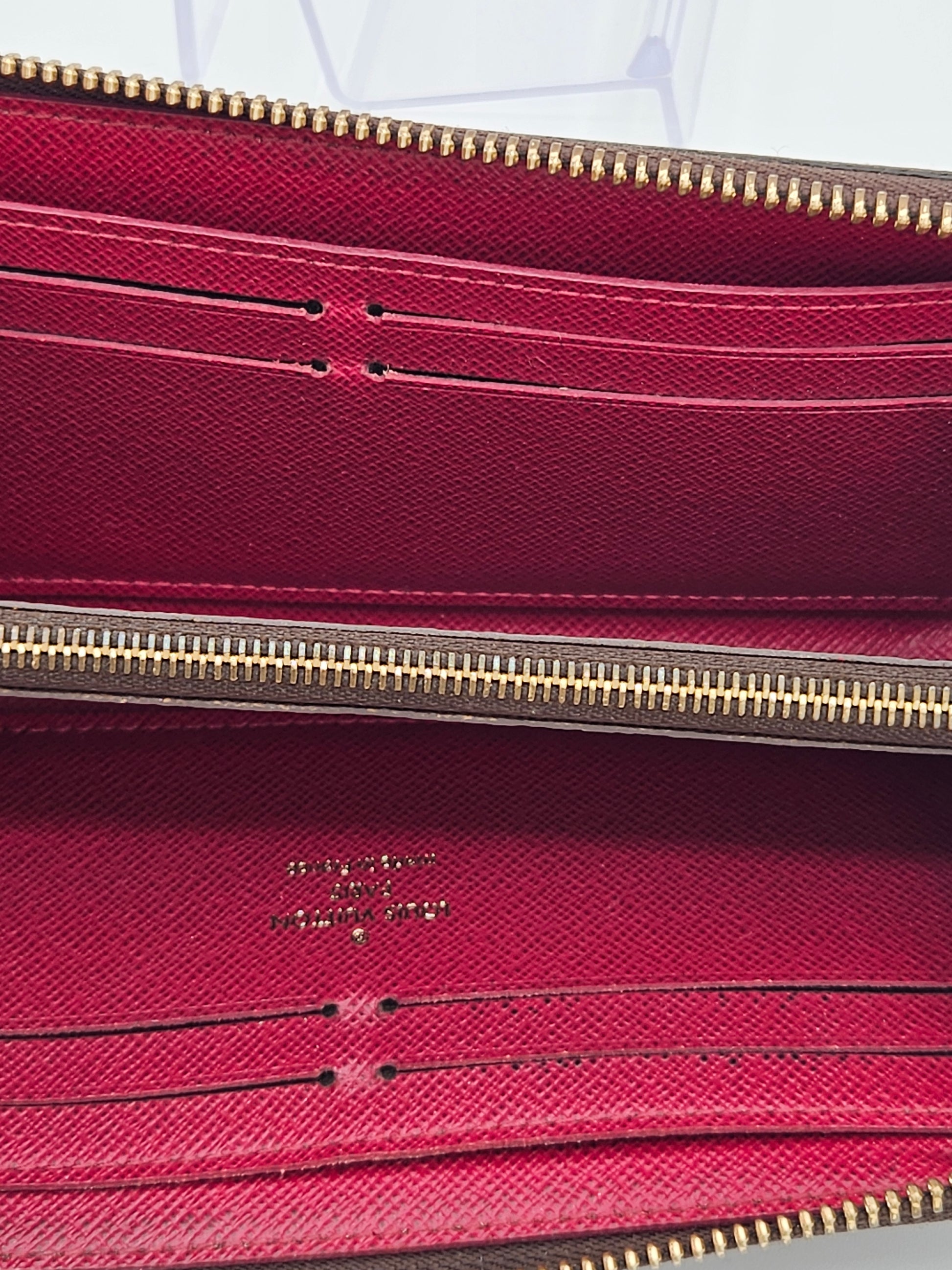 Close-up of a maroon wallet with gold zipper and brand logo.