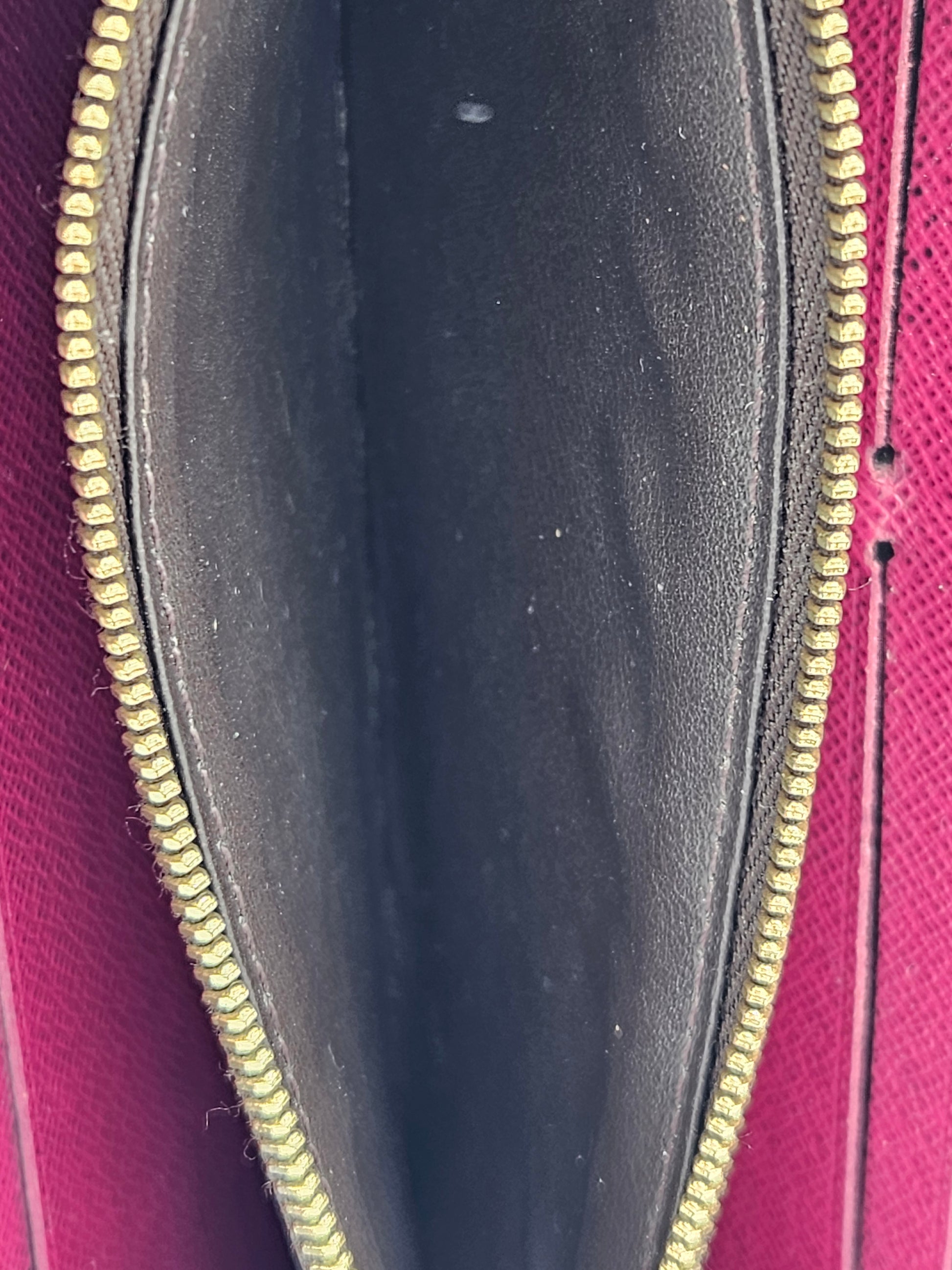 Close-up of a black wallet with gold zipper on a pink background