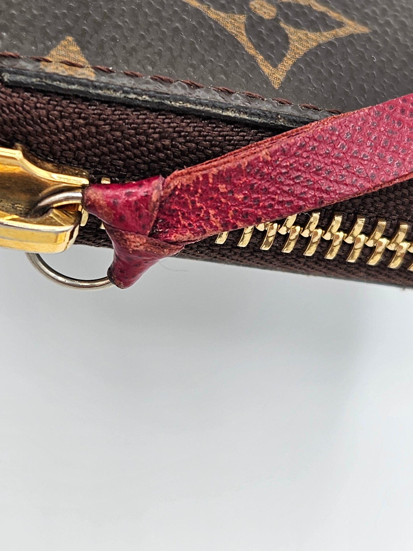 Close-up of a Louis Vuitton wallet with a red zipper and gold hardware on a light gray background.