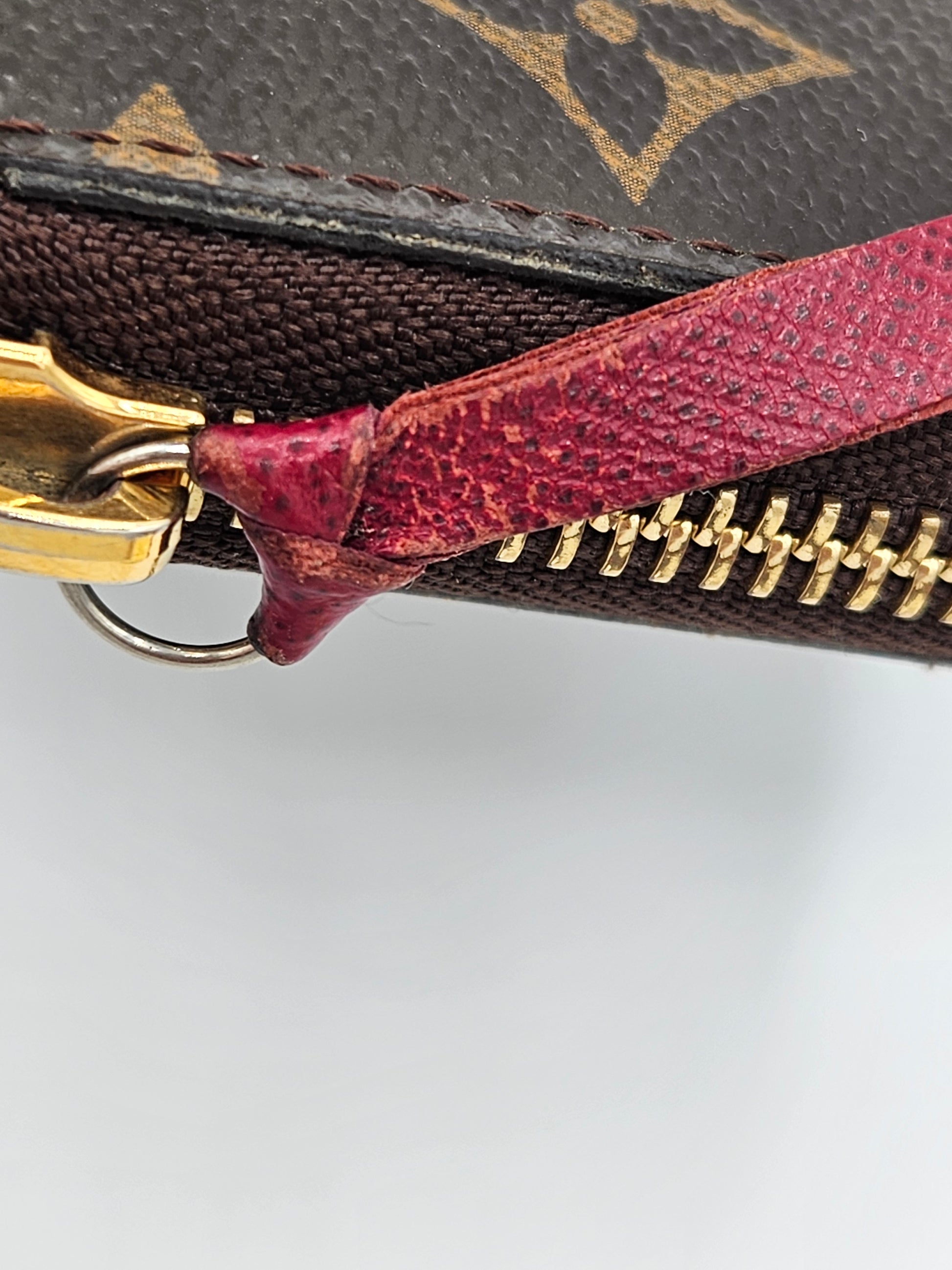 Close-up of a Louis Vuitton wallet with a red zipper and gold hardware on a light gray background.