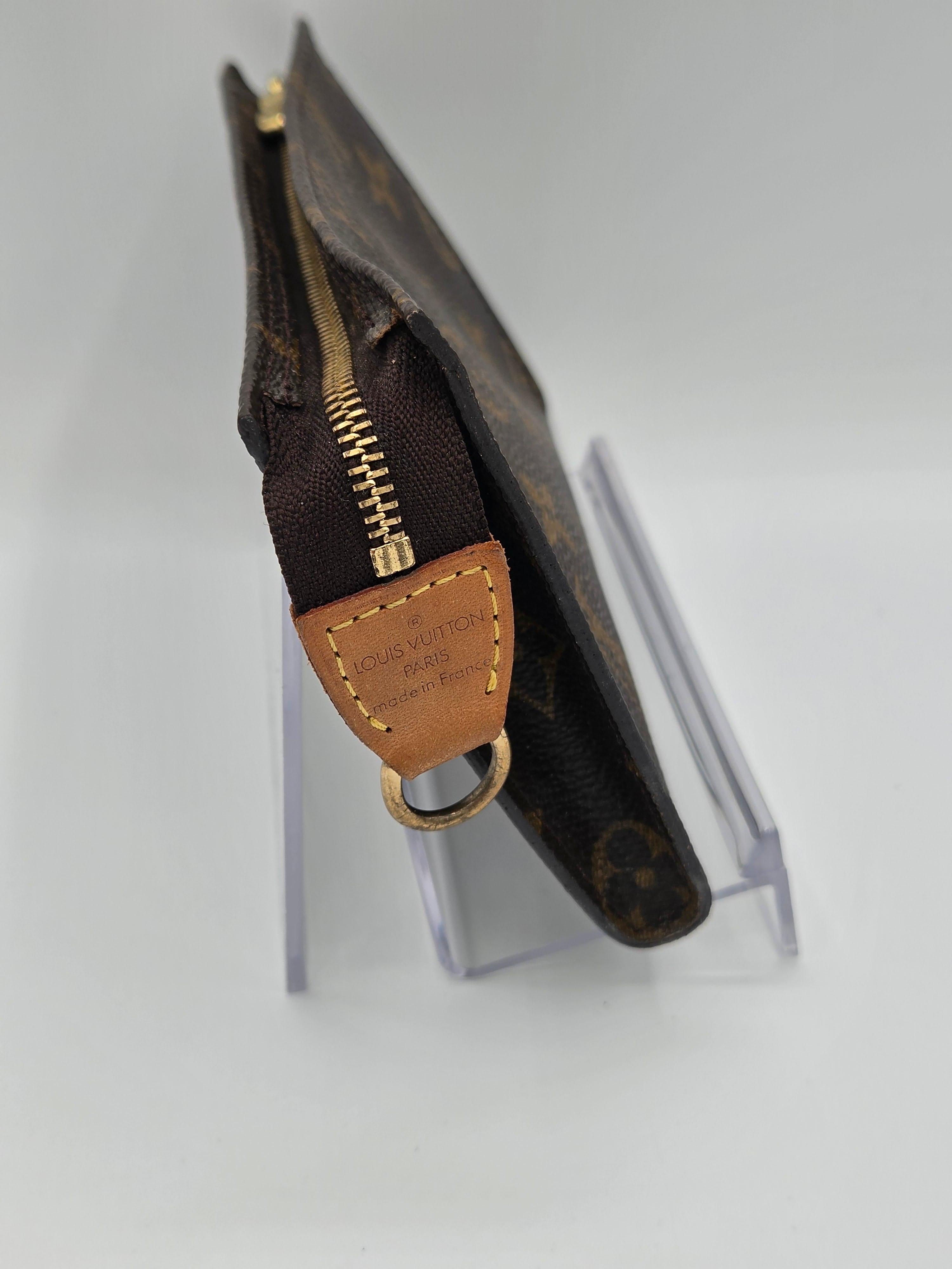 Brown leather keychain with gold zipper on a clear stand against a light gray background