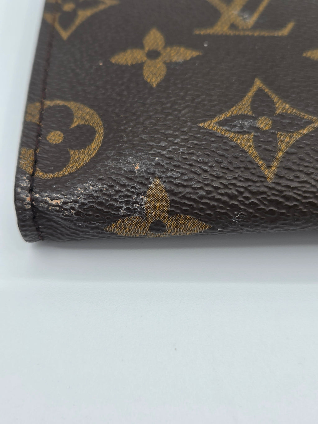 Close-up of a Louis Vuitton wallet corner with visible wear on a white background