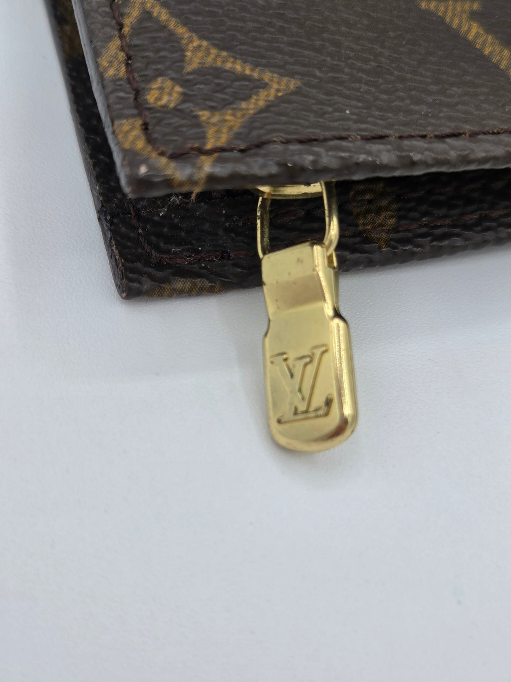 Close-up of a gold zipper pull on a Louis Vuitton bag with monogram pattern.