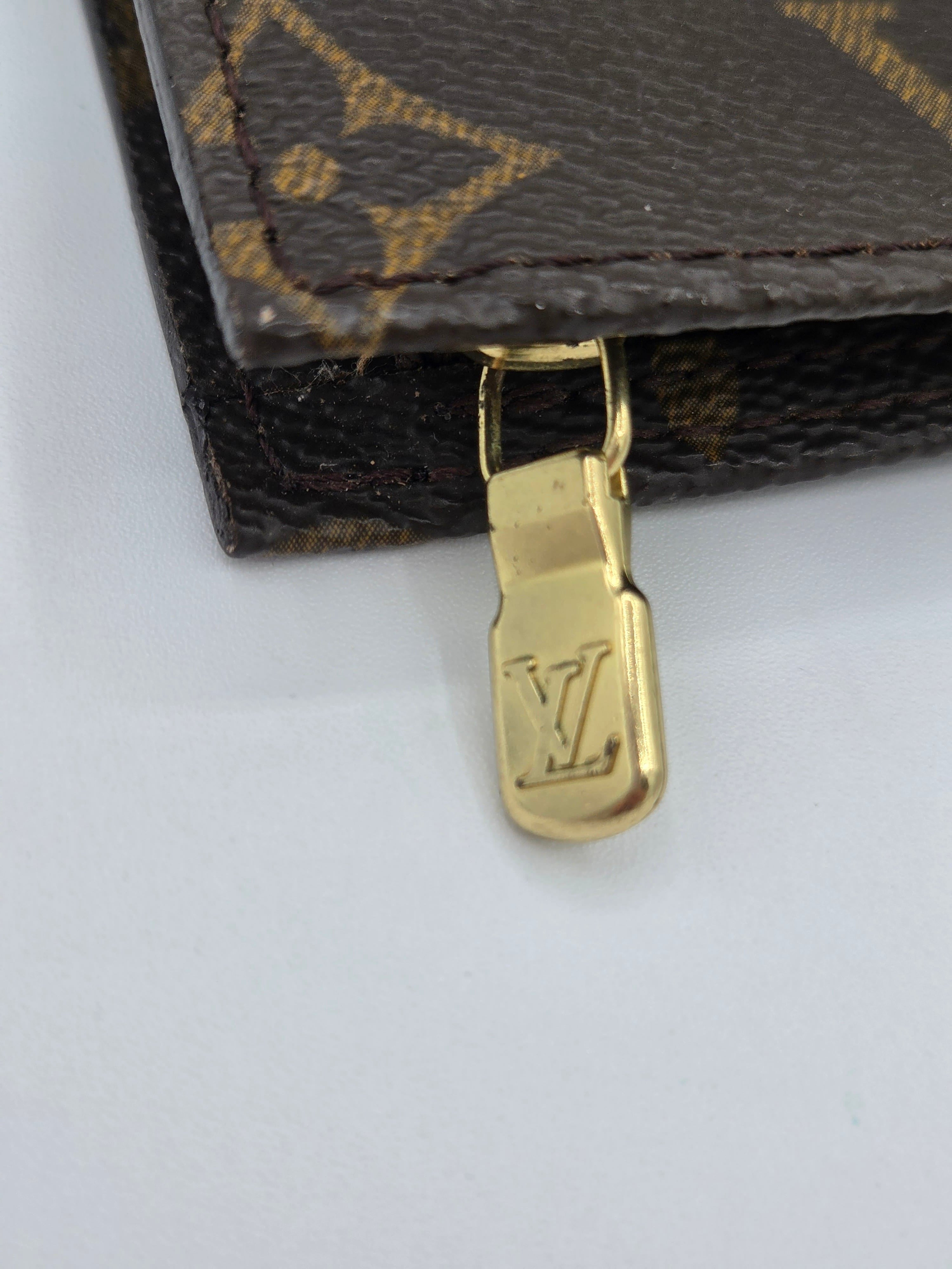 Close-up of a gold zipper pull on a Louis Vuitton bag with monogram pattern.