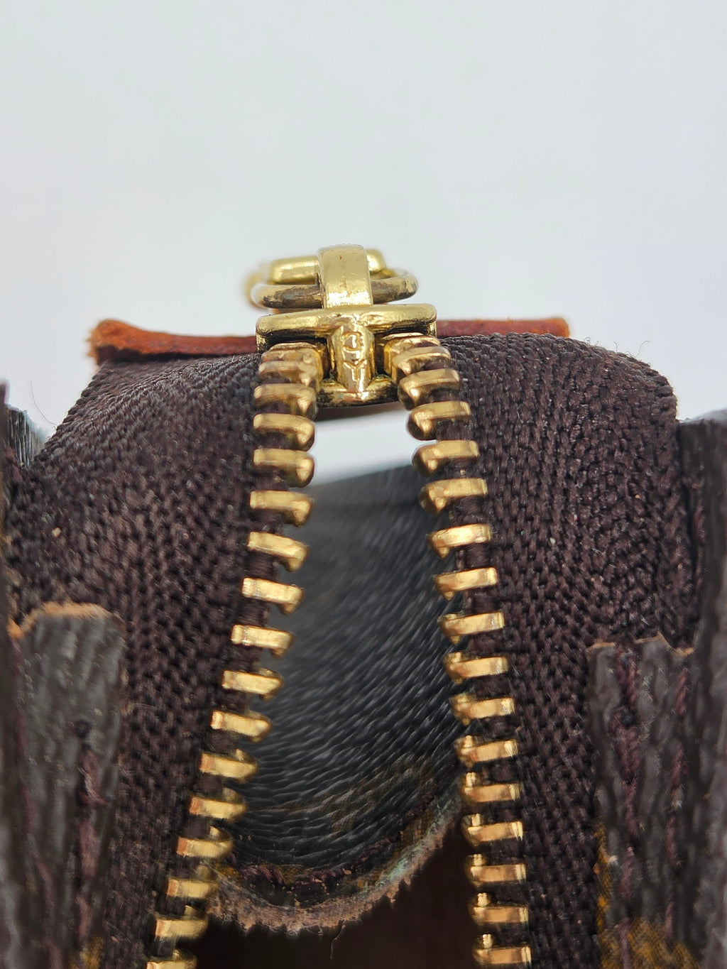 Close-up of a gold zipper on a brown textured fabric background