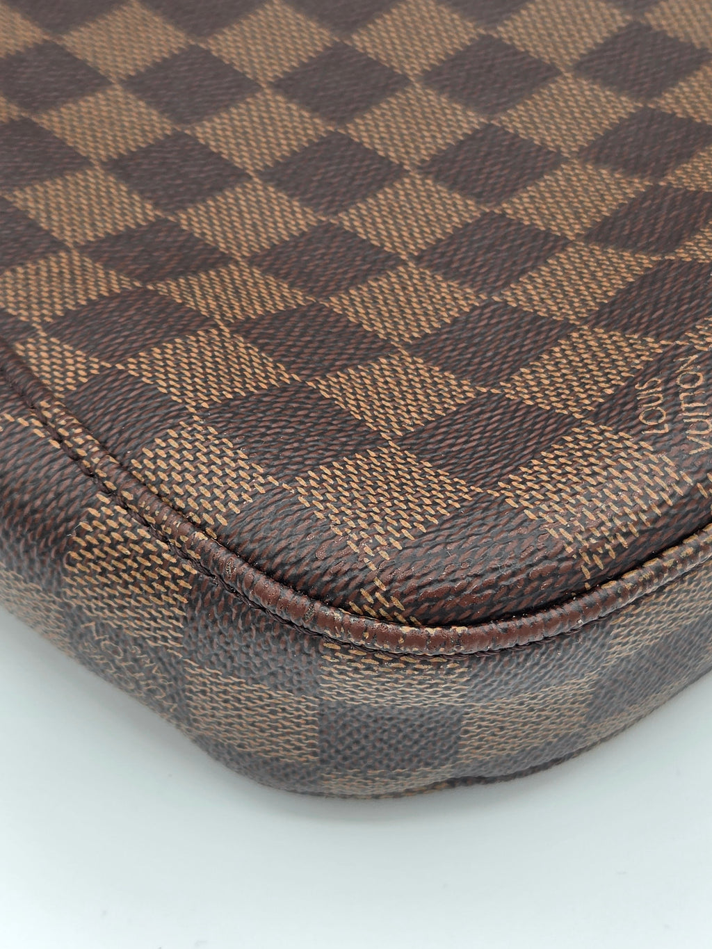 Close-up of a brown and beige checkered fabric with a brand logo on a white background