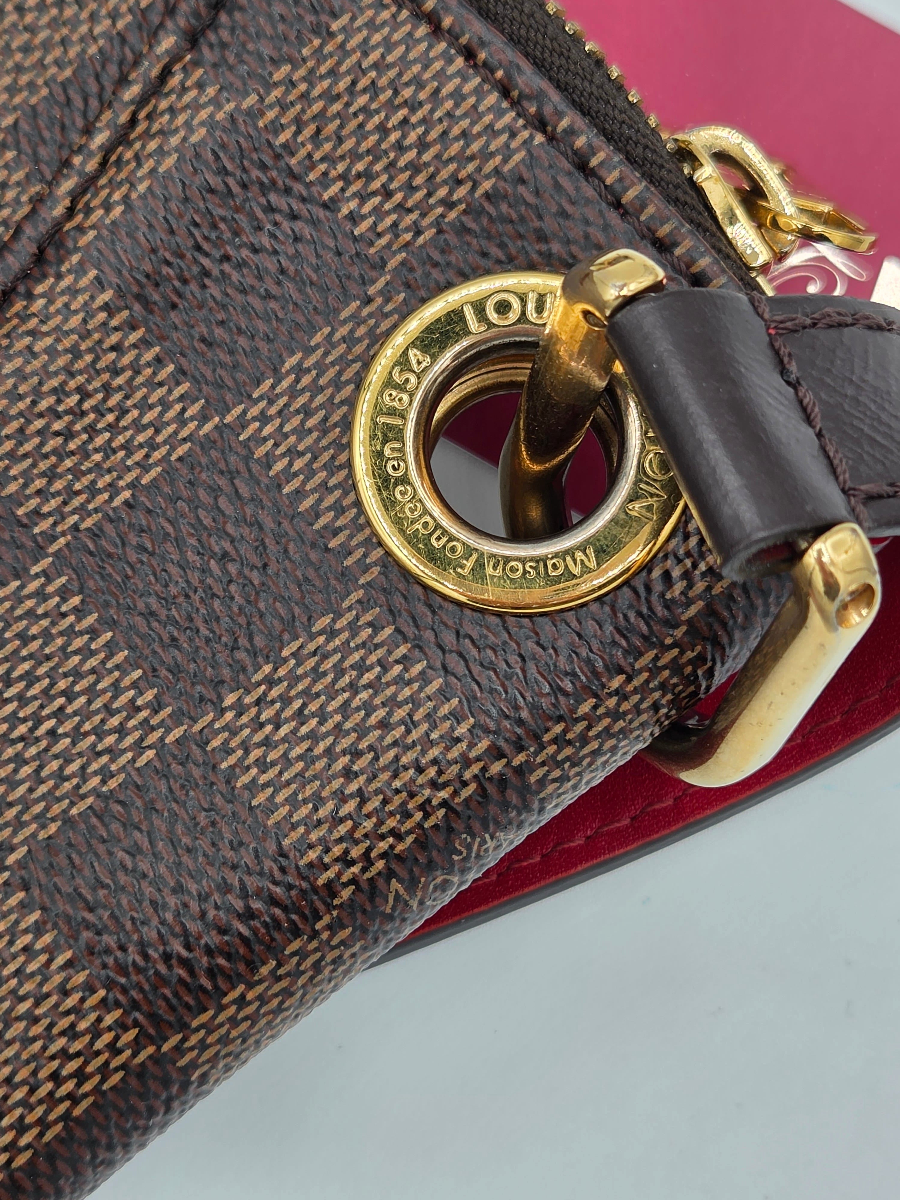 Close-up of a Louis Vuitton handbag with gold lock and checkered pattern.