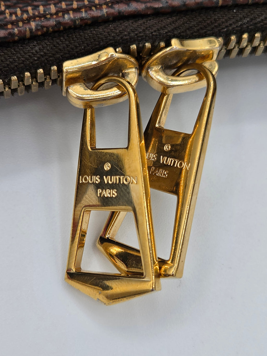 Gold zipper pull with Louis Vuitton branding on a gray background