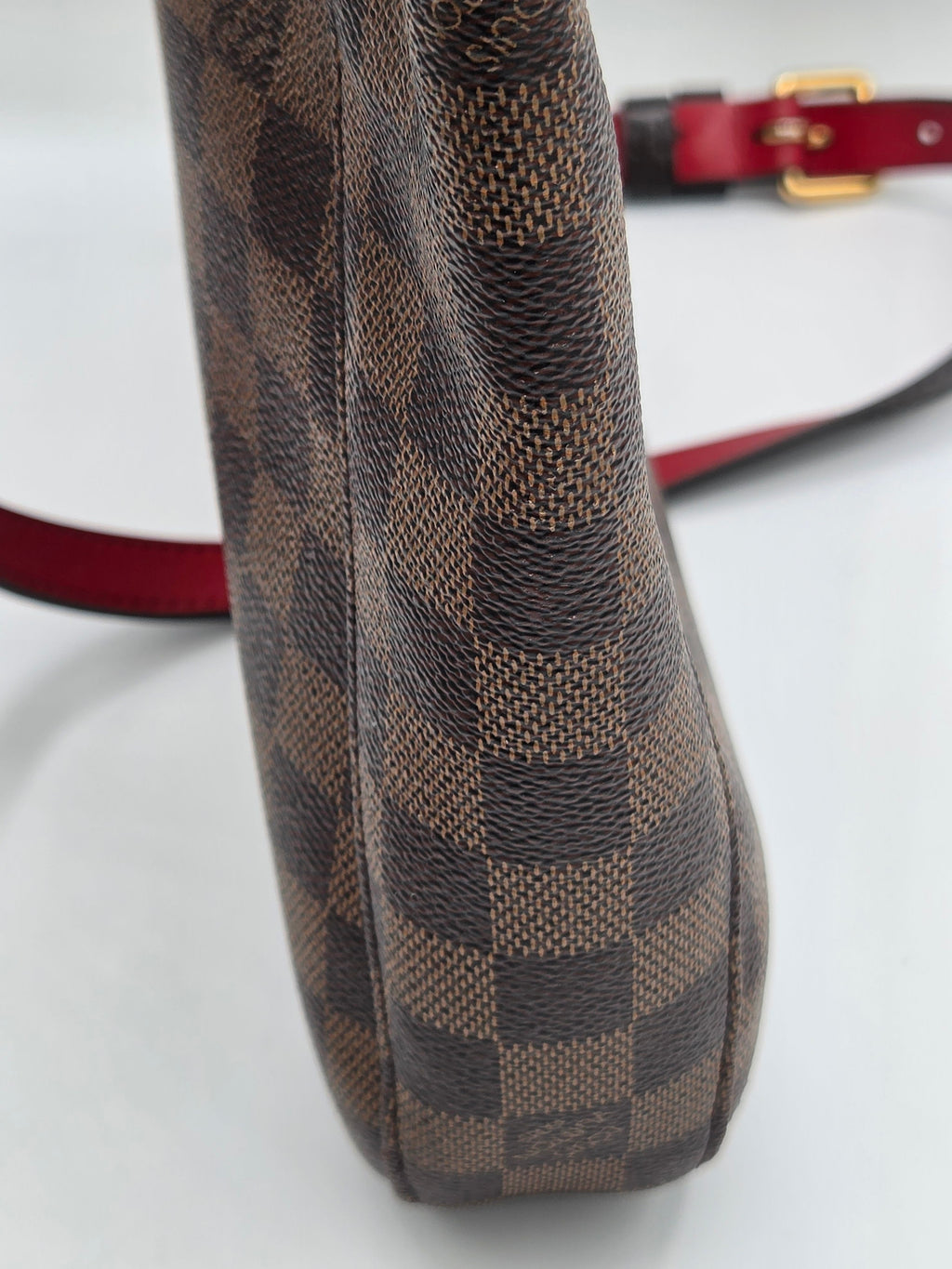 Brown checkered handbag with a red strap on a white background