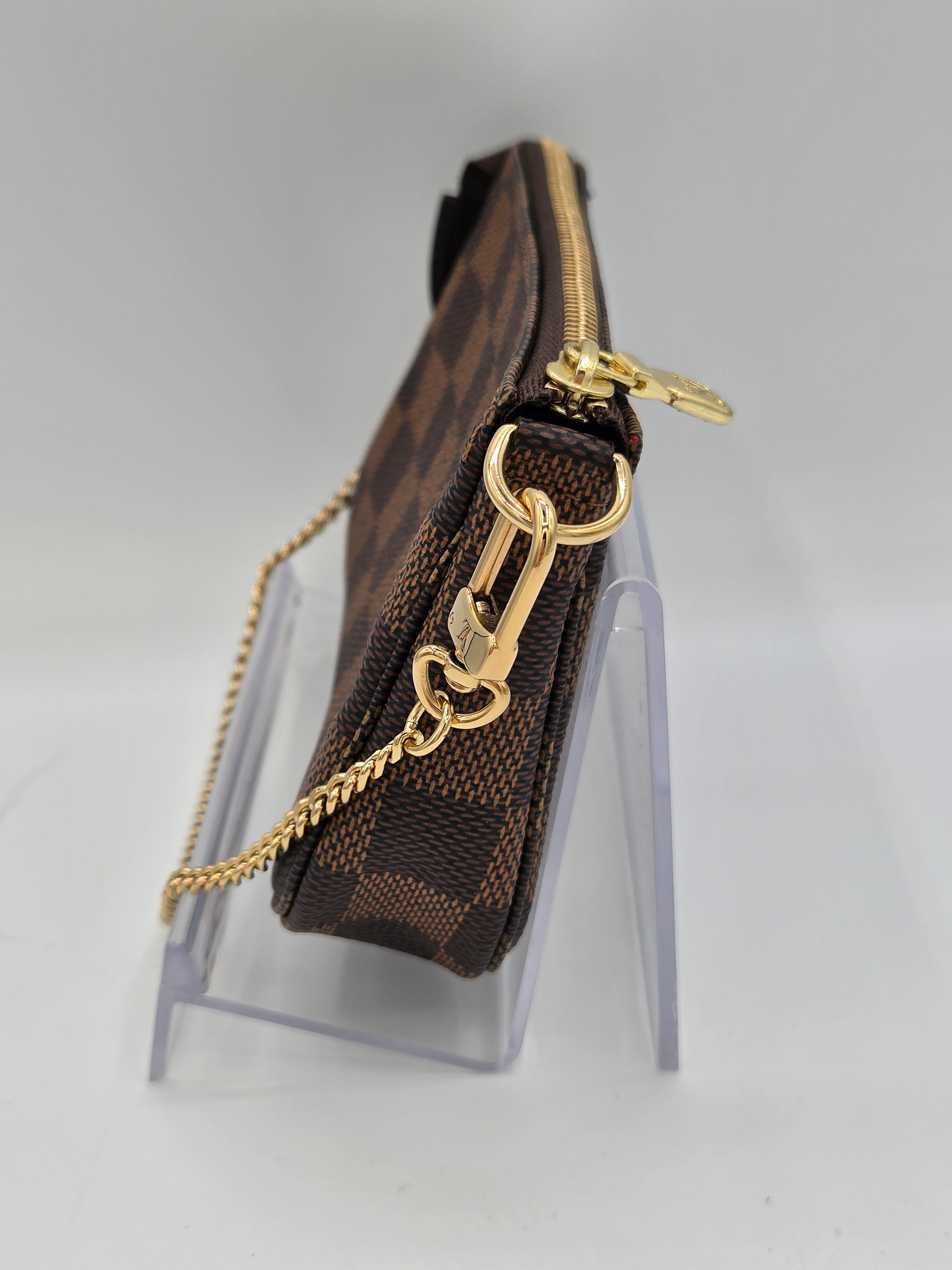 Brown pouch with gold chain and clasp on a clear stand against a light gray background