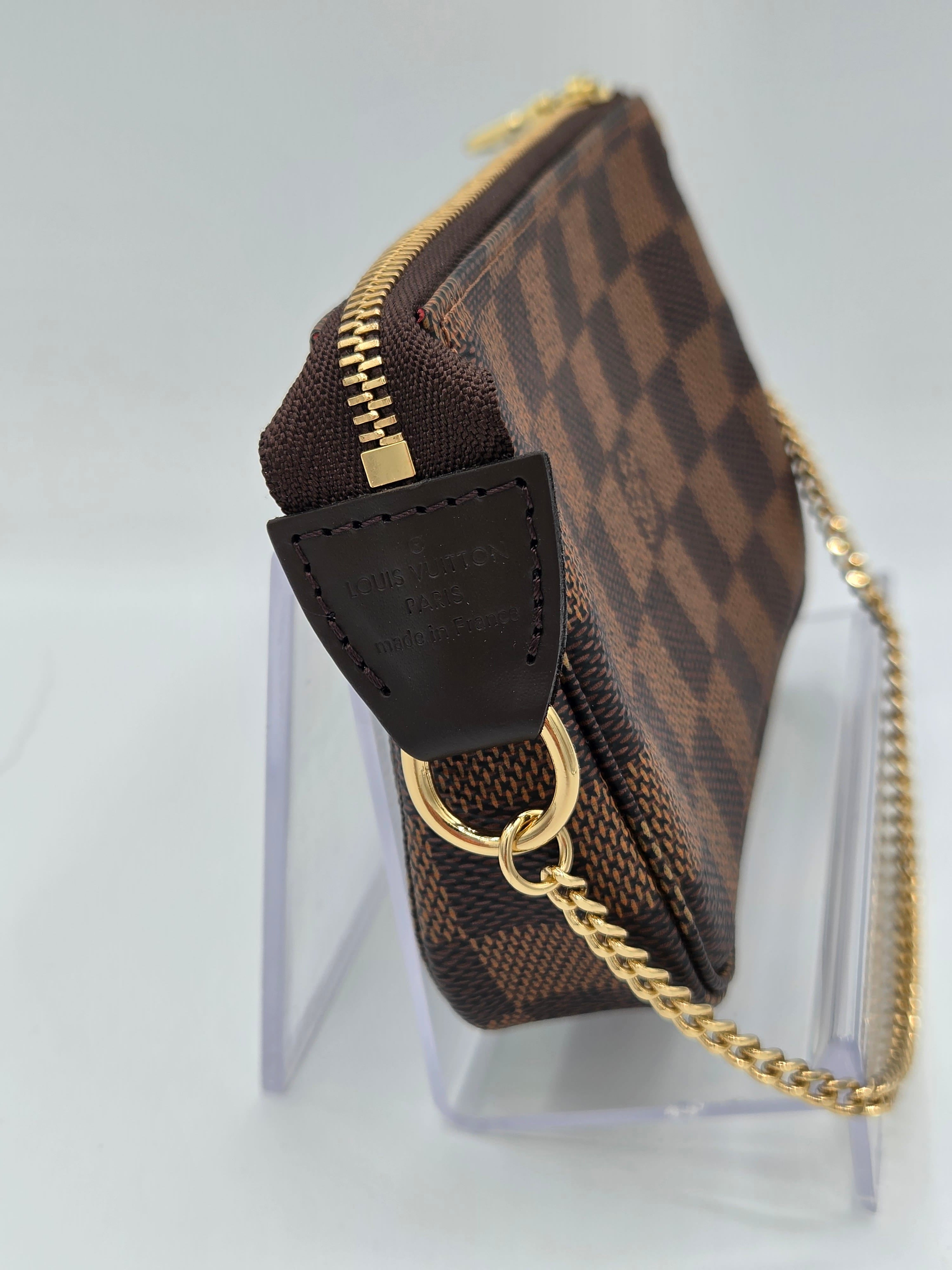Designer handbag with gold chain and checkered pattern on a clear stand