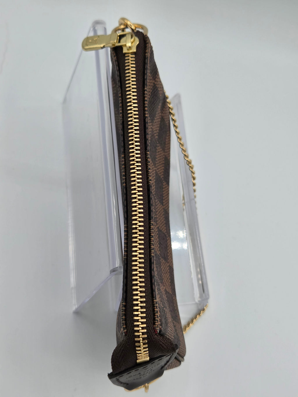 Designer handbag with gold zipper on a clear stand against a white background