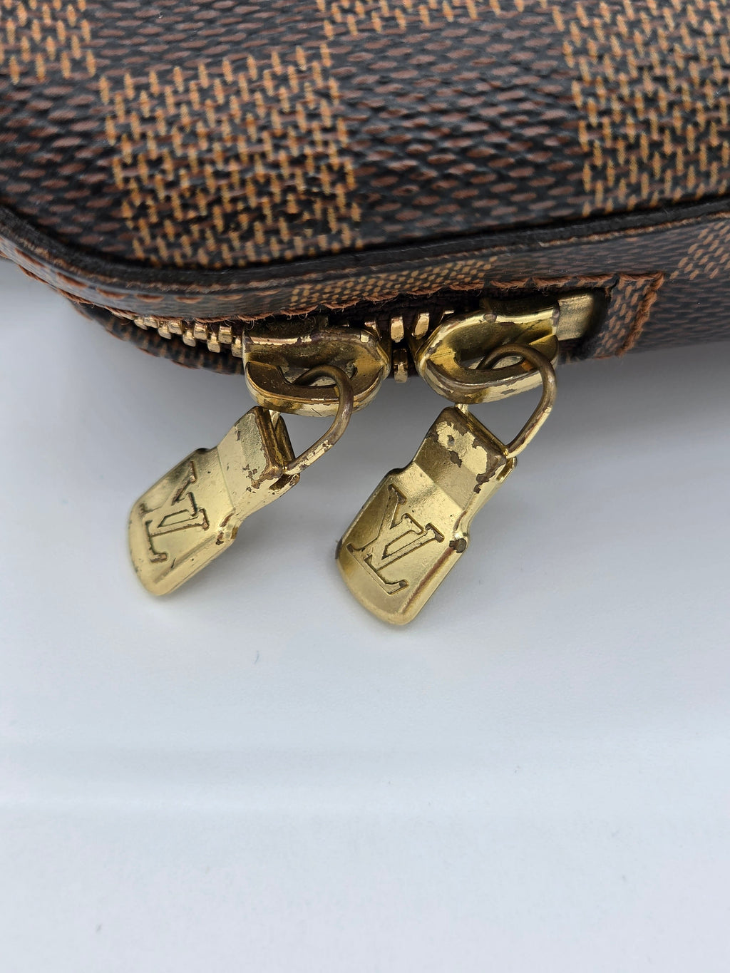 Close-up of a brown textured bag with gold zipper pulls on a light gray background
