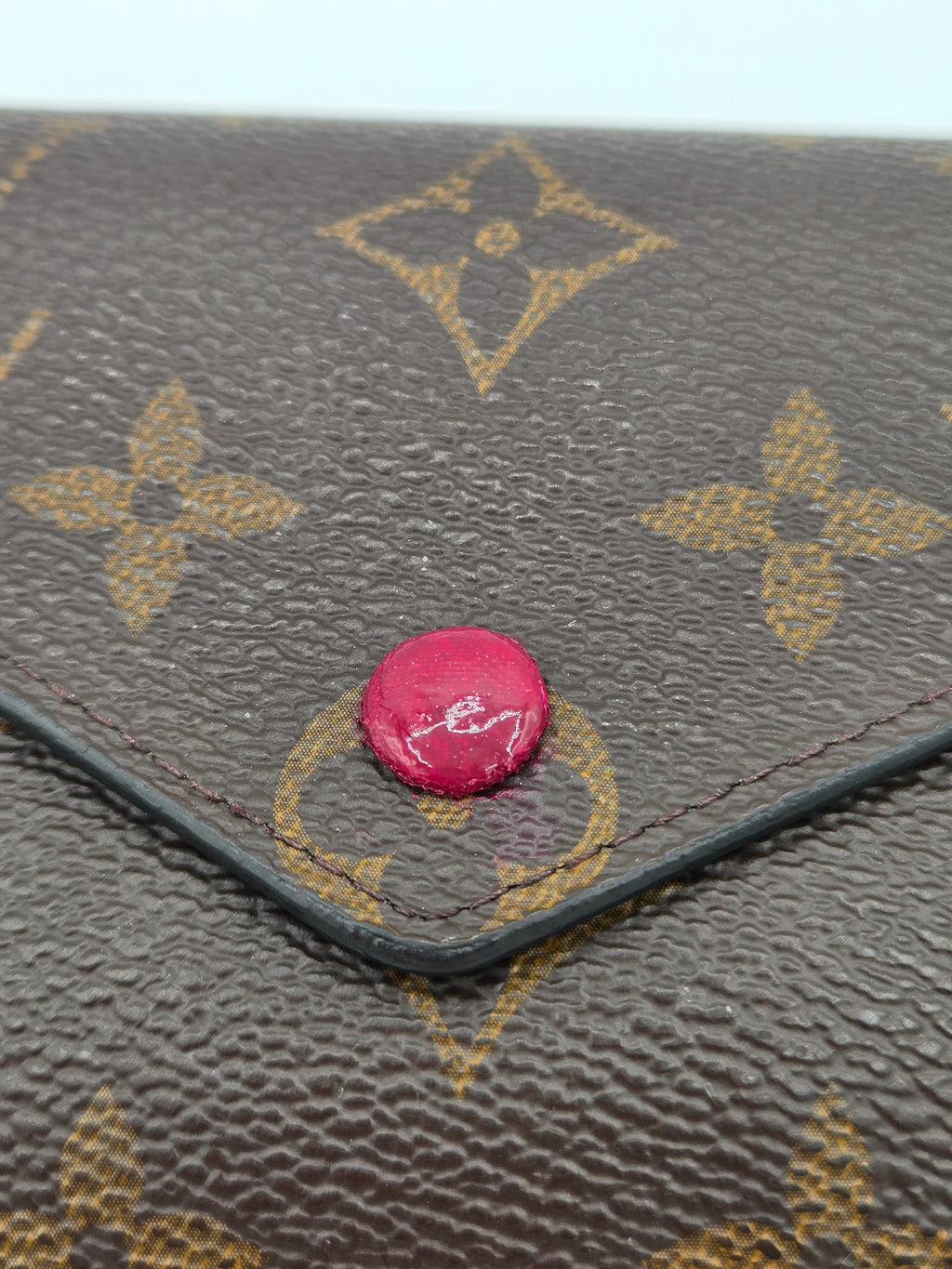 Louis Vuitton handbag with a pink button on a textured background