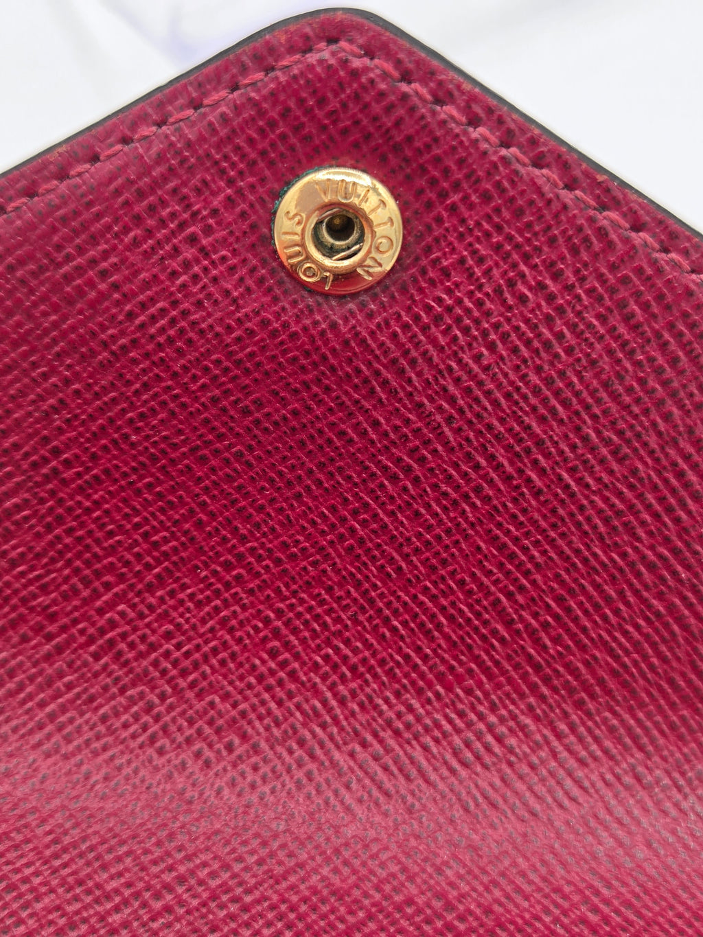 Close-up of a red textured wallet with a gold logo on a white background