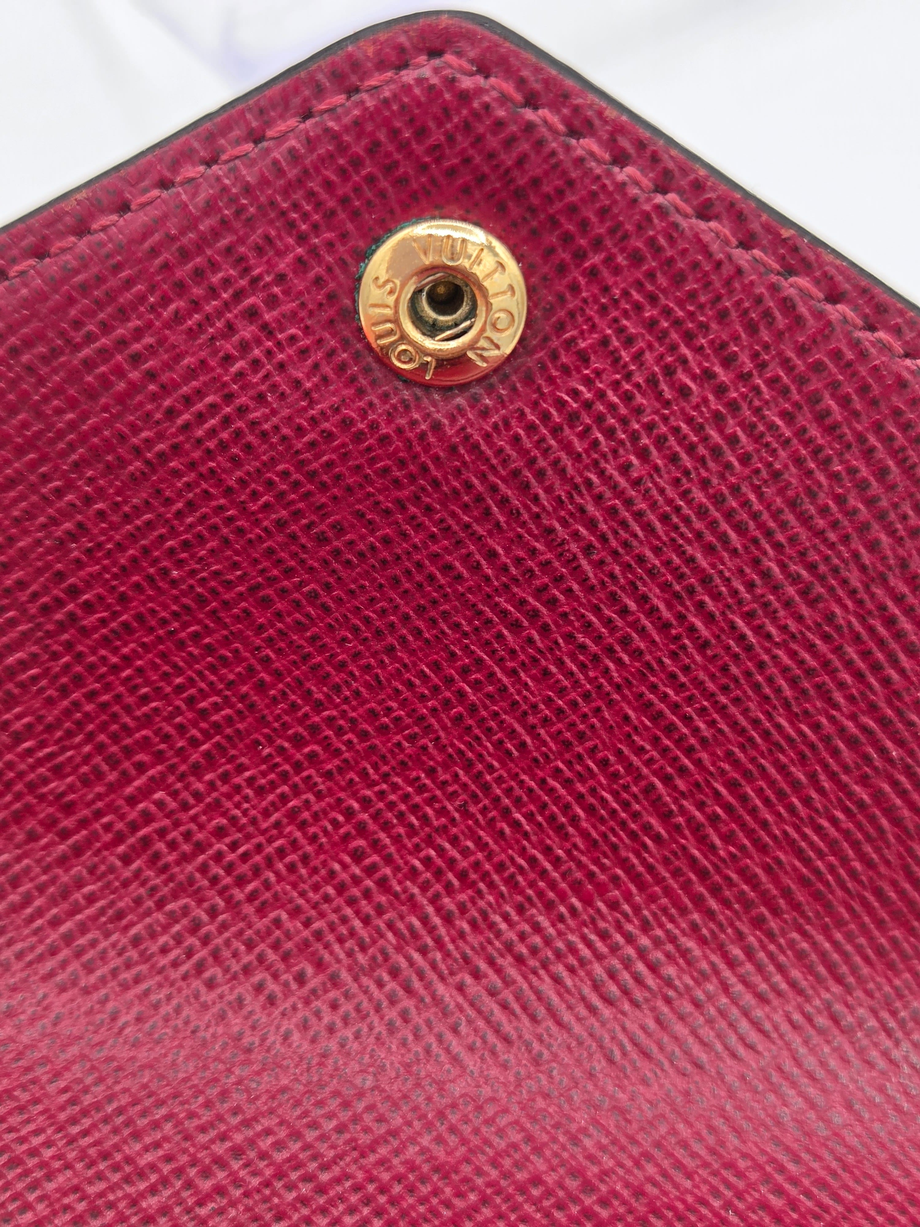 Close-up of a red textured wallet with a gold logo on a white background