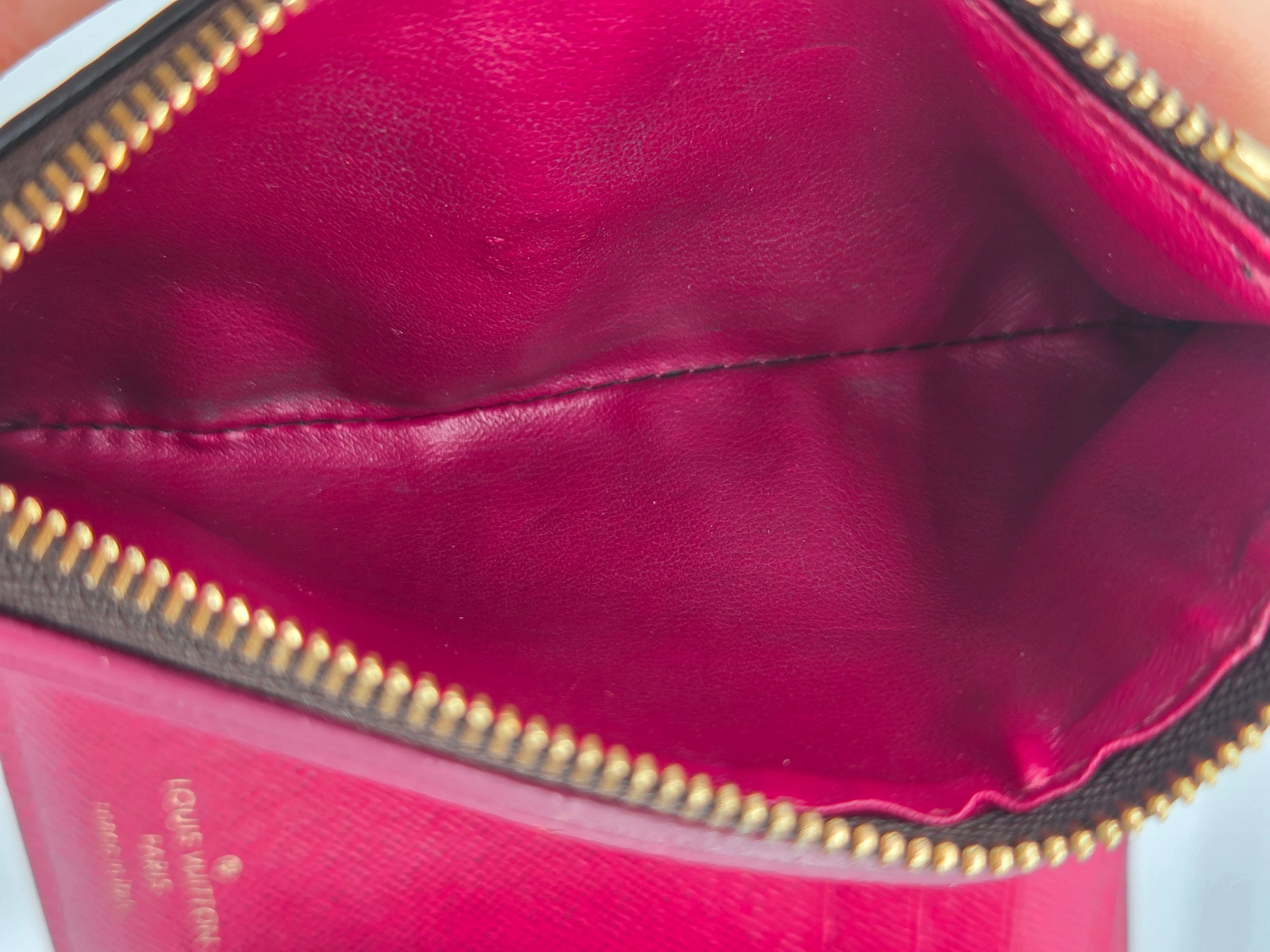 Close-up of a red handbag with gold zipper, brand name visible.