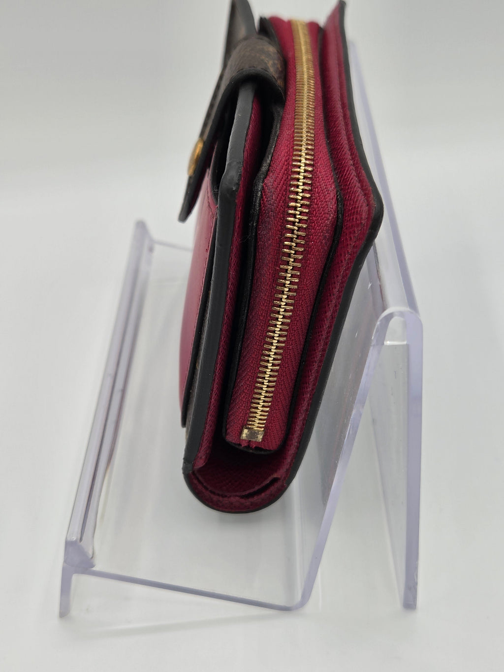 Maroon wallet with gold zipper on a clear stand against a white background
