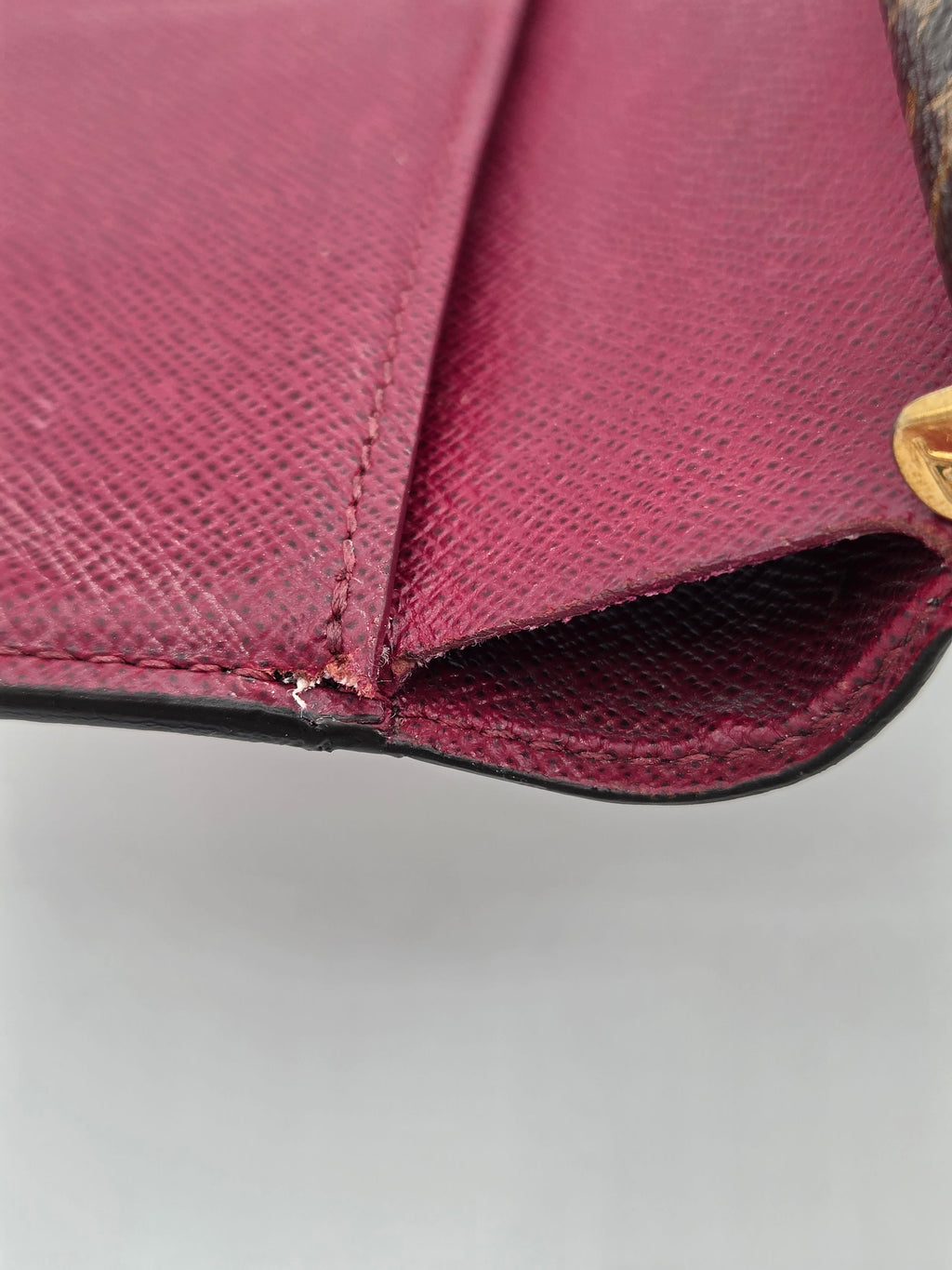 Close-up of a maroon handbag with a gold clasp on a gray background
