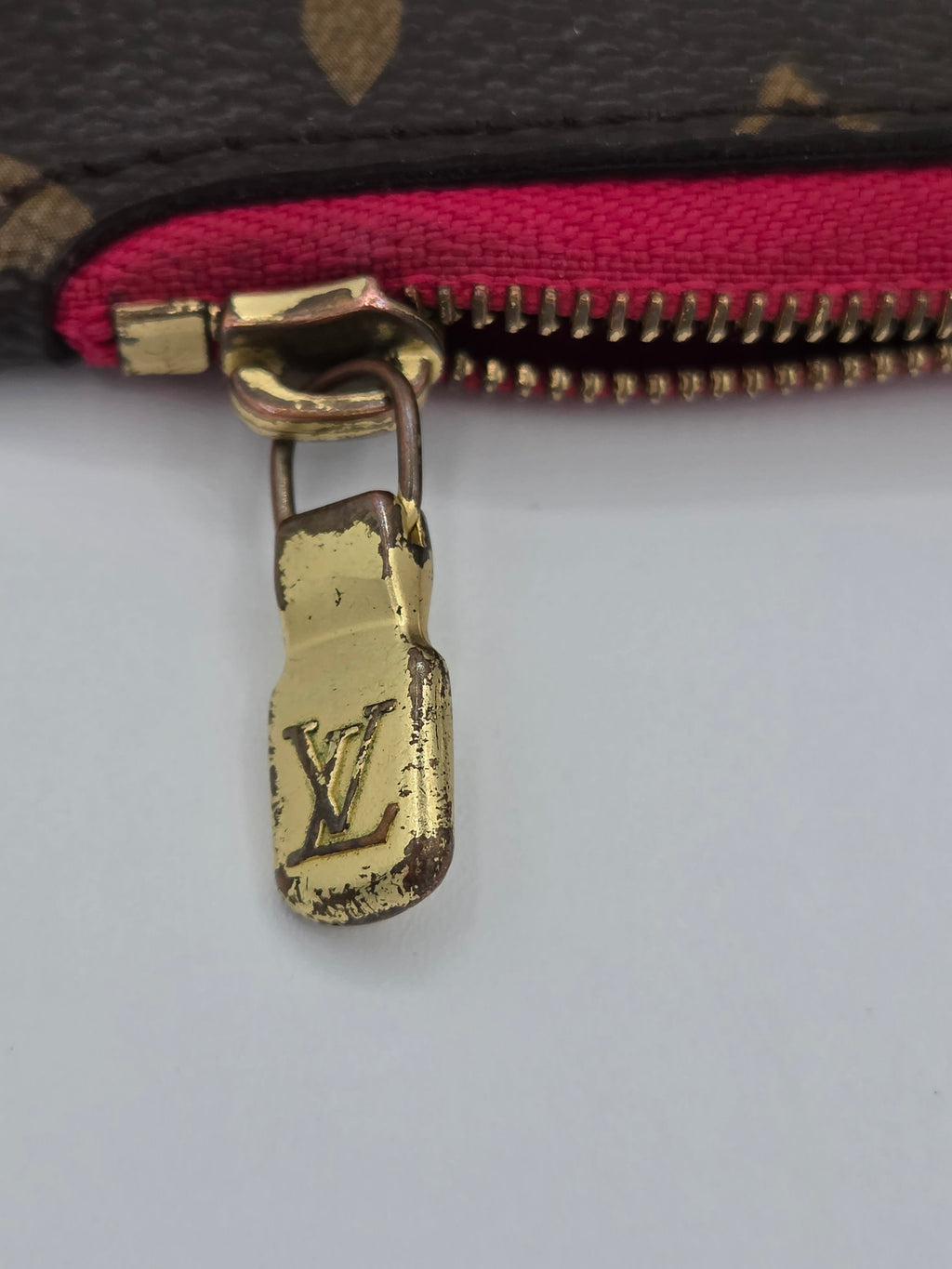 Close-up of a gold zipper pull with LV logo on a patterned bag.