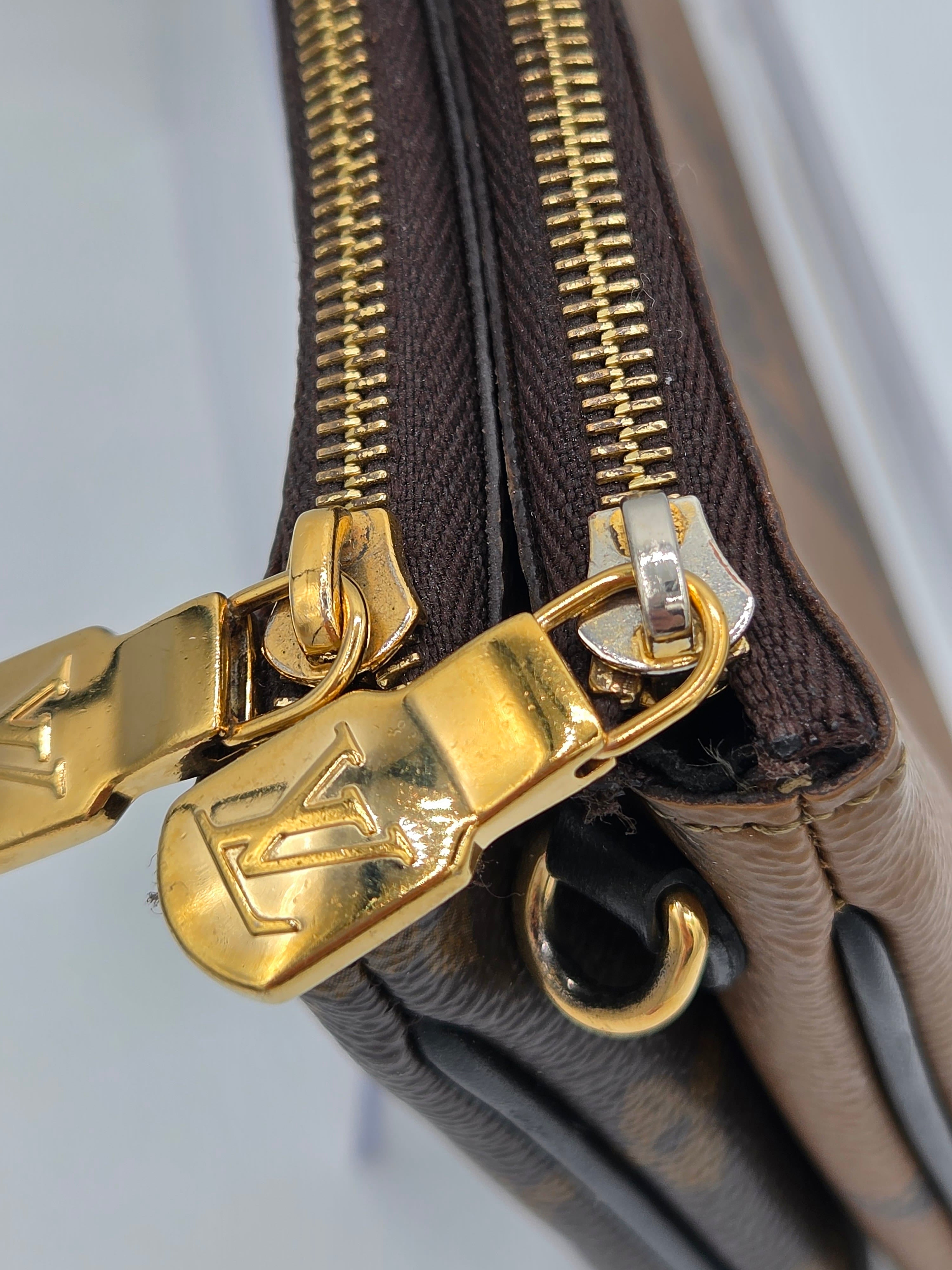 Close-up of a brown leather handbag with gold zipper and logo, on a light gray background.